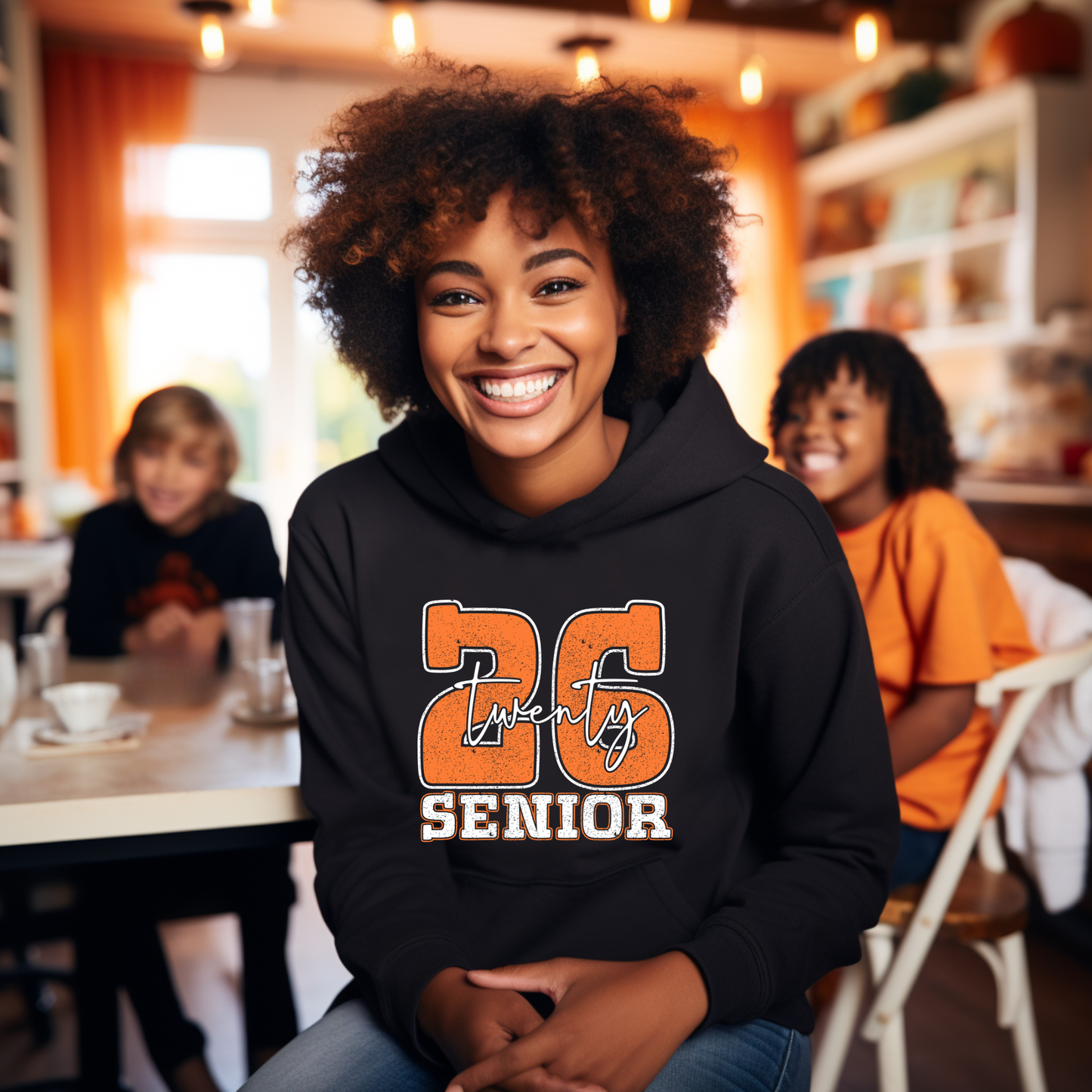 Person wearing a black hoodie with '26 Twenty Six Senior' text in a casual indoor setting.