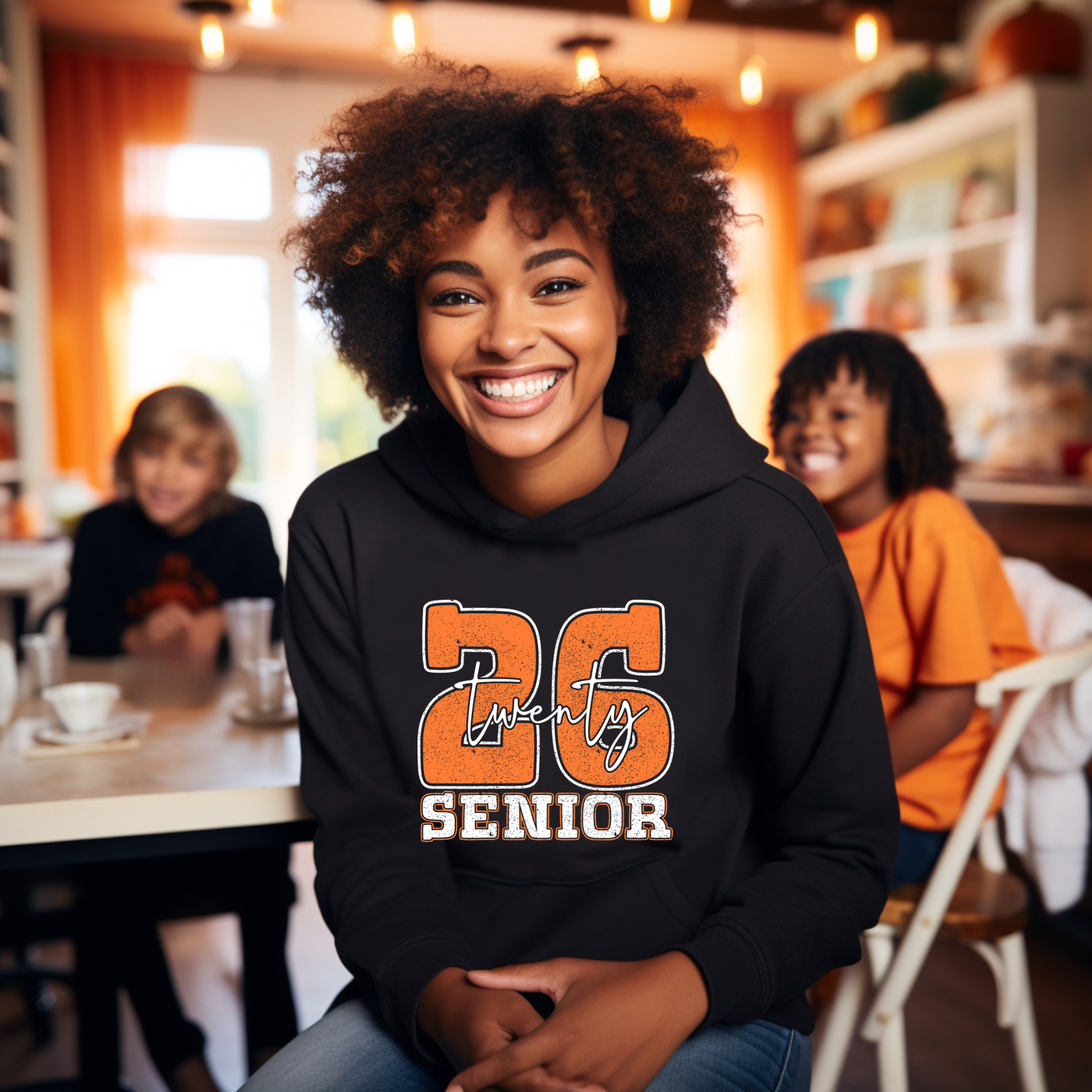Person wearing a black hoodie with '26 Twenty Six Senior' text in a casual indoor setting.