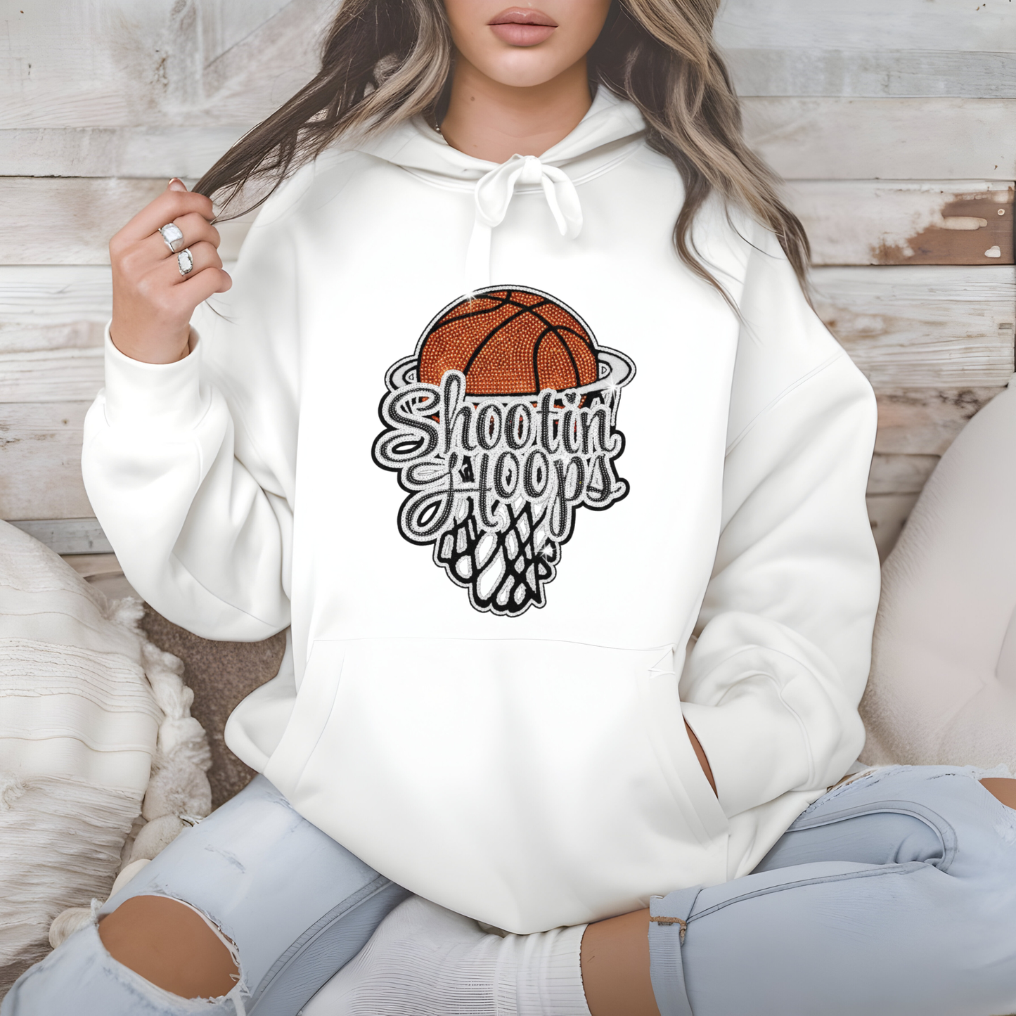 Person wearing a white hoodie with a basketball graphic and text, sitting on a wooden floor.