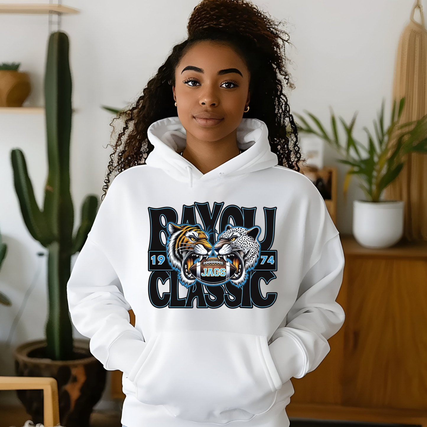Person wearing a white hoodie with a tiger and panther design and text in a room with plants.