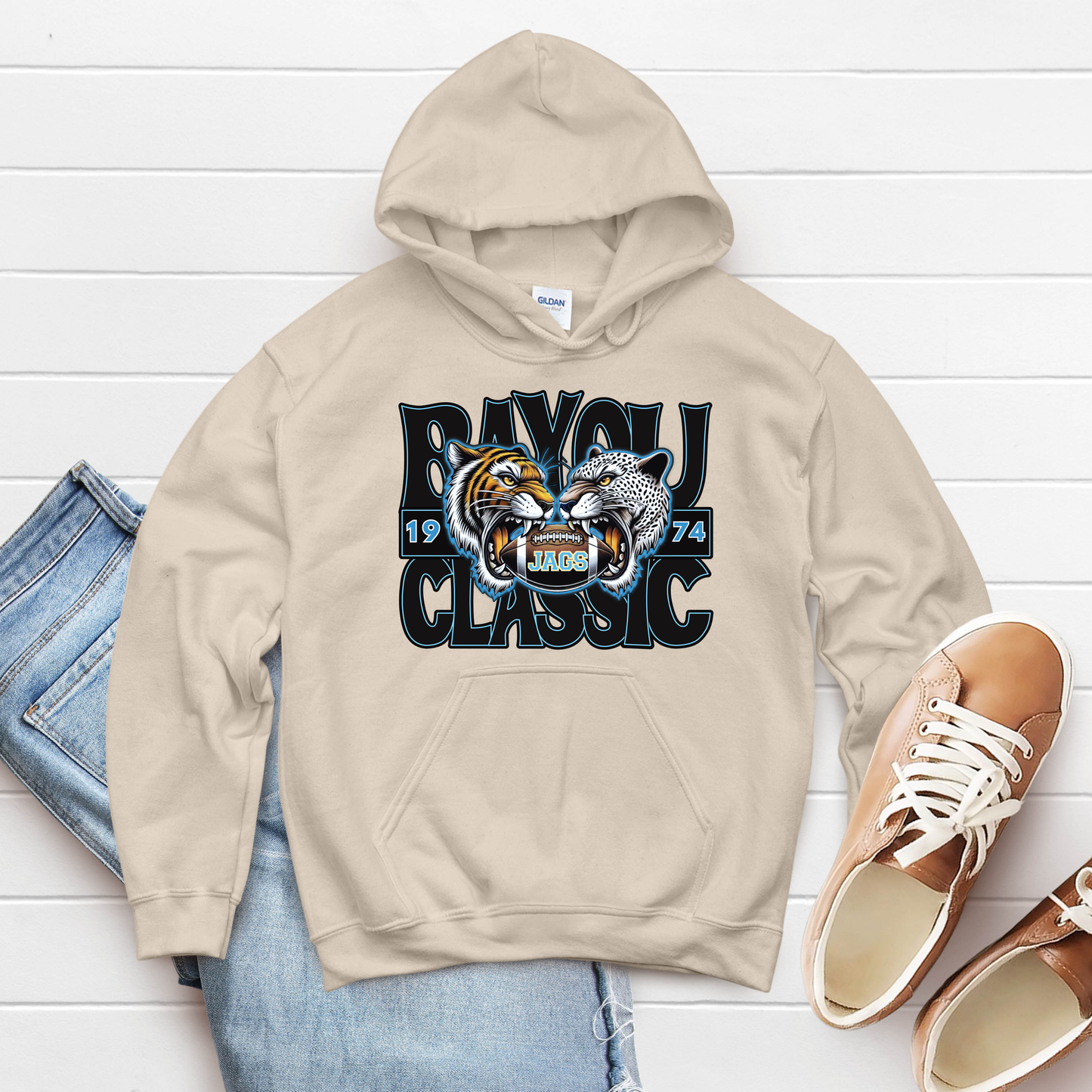 Beige hoodie with 'Ravoli Classic' design on a white wooden surface with jeans and shoes.