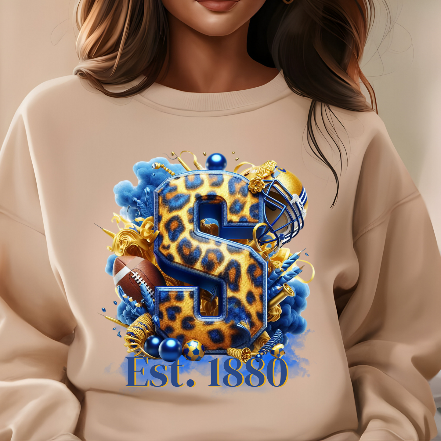 A close-up of a person wearing a beige sweatshirt with a large graphic print. The design features a stylized leopard-print letter 'S' in blue and gold, surrounded by football helmets, a football, blue smoke effects, and the text 'Est.