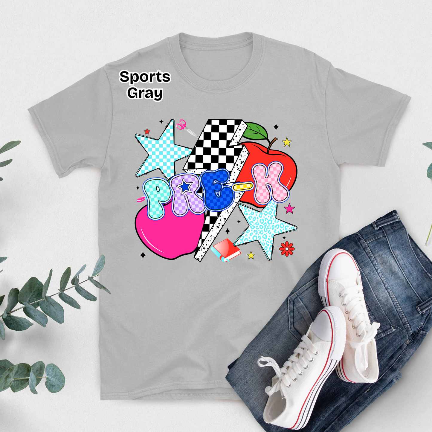 A light gray graphic T-shirt laid flat with blue jeans and white sneakers beside it on a white surface. The shirt has a colorful school-themed graphic with the word 'P.