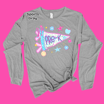 A heather gray long-sleeve t-shirt with a distressed graphic of a pink and blue pennant flag that reads 'PRE-K' surrounded by stars, flowers, and a pink ribbon. The shirt is displayed on a solid bright pink background with a 'Sports Gray' text overlay near the collar.