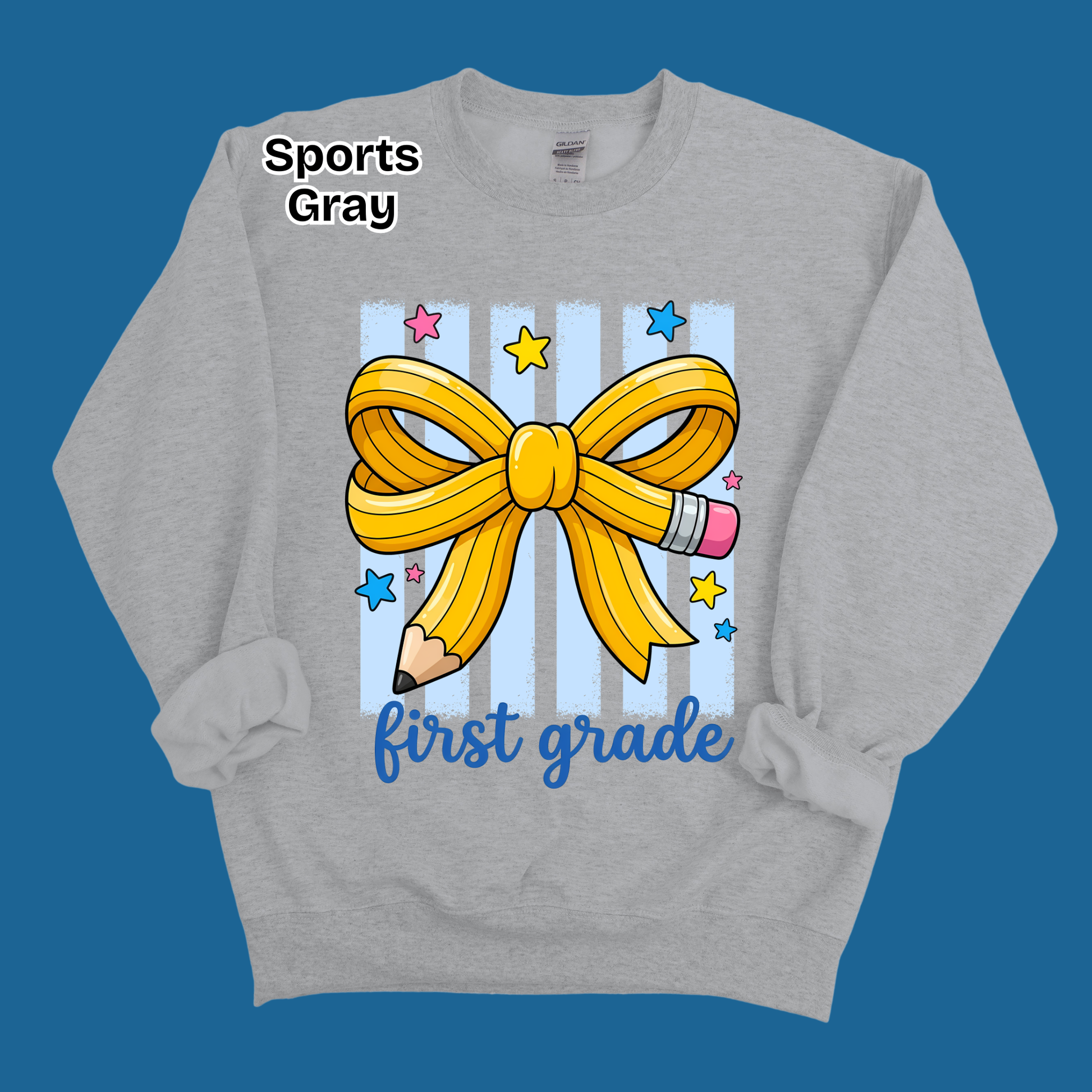 A heather gray sweatshirt with a 'first grade' first birthday graphic, featuring a yellow ribbon bow, pencil, and stars on a blue striped background, displayed on a solid blue background.
