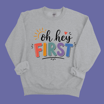 A light gray crewneck sweatshirt featuring a colorful graphic that reads 'Kinder Garten' in a playful, patterned font with a pink bow underneath, displayed against a solid blue background.
