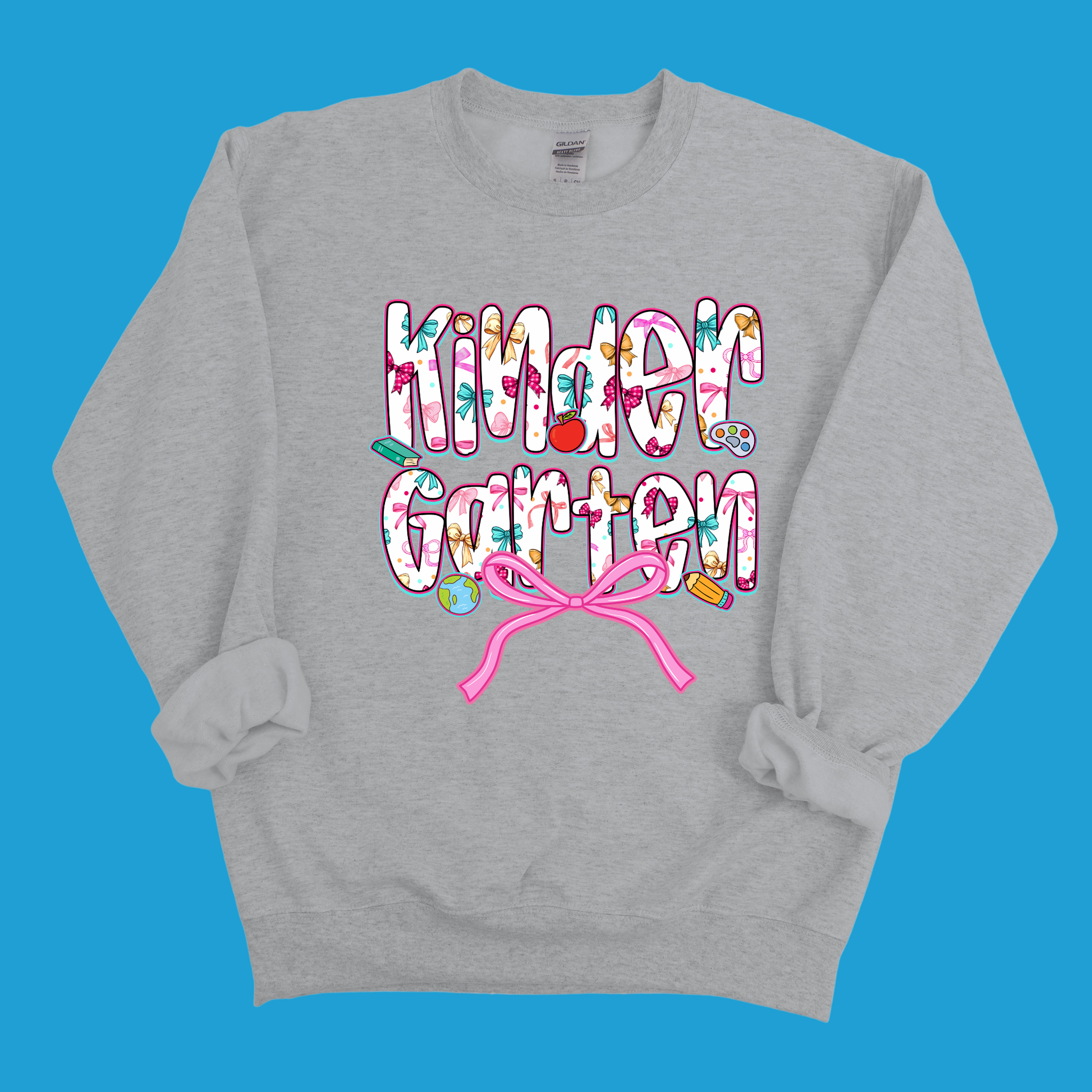 A light gray crewneck sweatshirt featuring a colorful graphic that reads 'Kinder Garten' in a playful, patterned font with a pink bow underneath, displayed against a solid blue background.