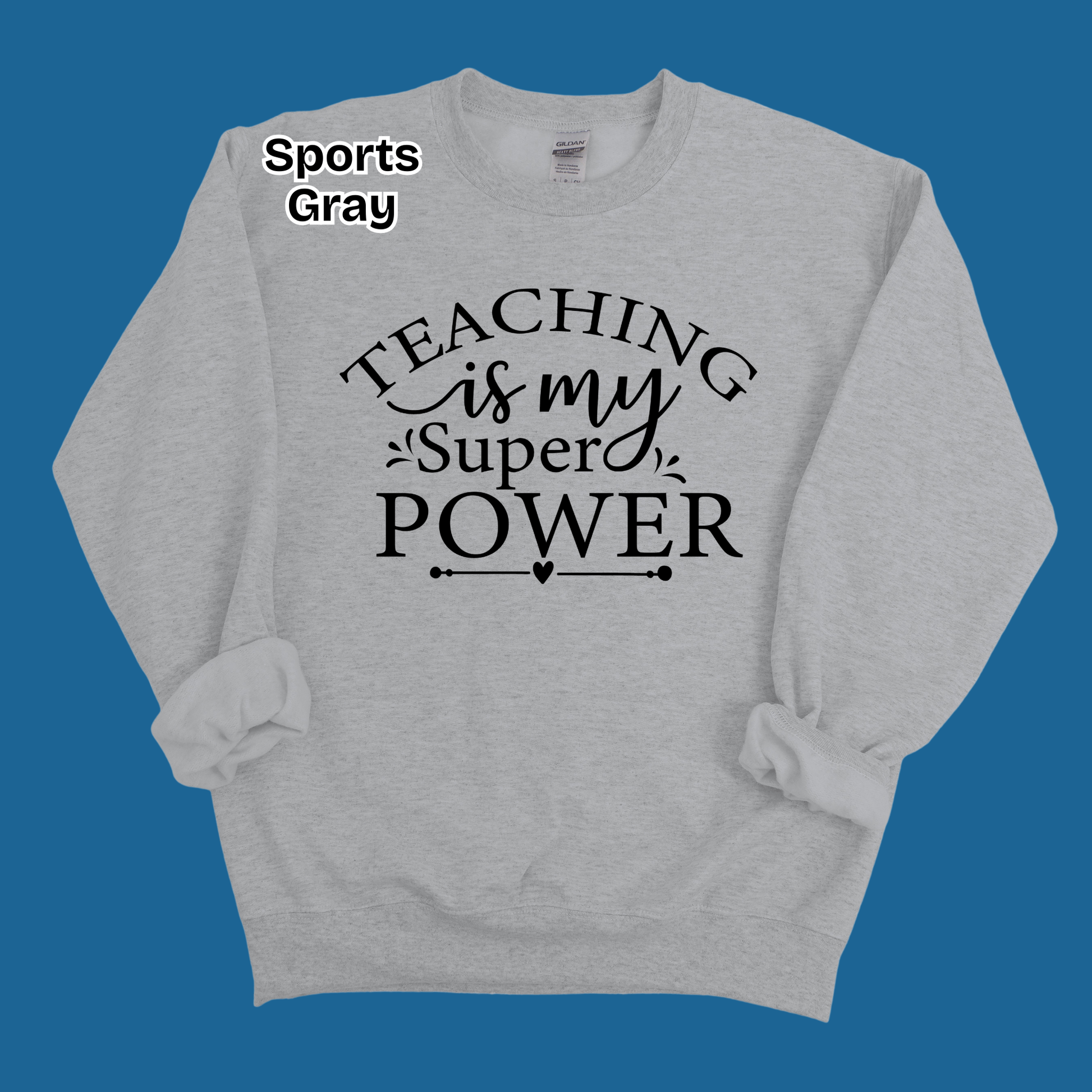 A light gray heather crewneck sweatshirt with rolled cuffs, featuring the black printed text 'TEACHING is my Super POWER' on the front. The text 'Sports Gray' is displayed in the top-left corner, indicating the color variant.