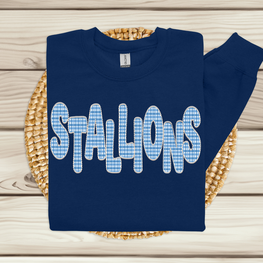 A navy blue sweatshirt with the word 'STALLIONS' printed across the chest in large white letters filled with a light blue and white gingham check pattern, displayed on a woven straw mat over a light wood plank background.