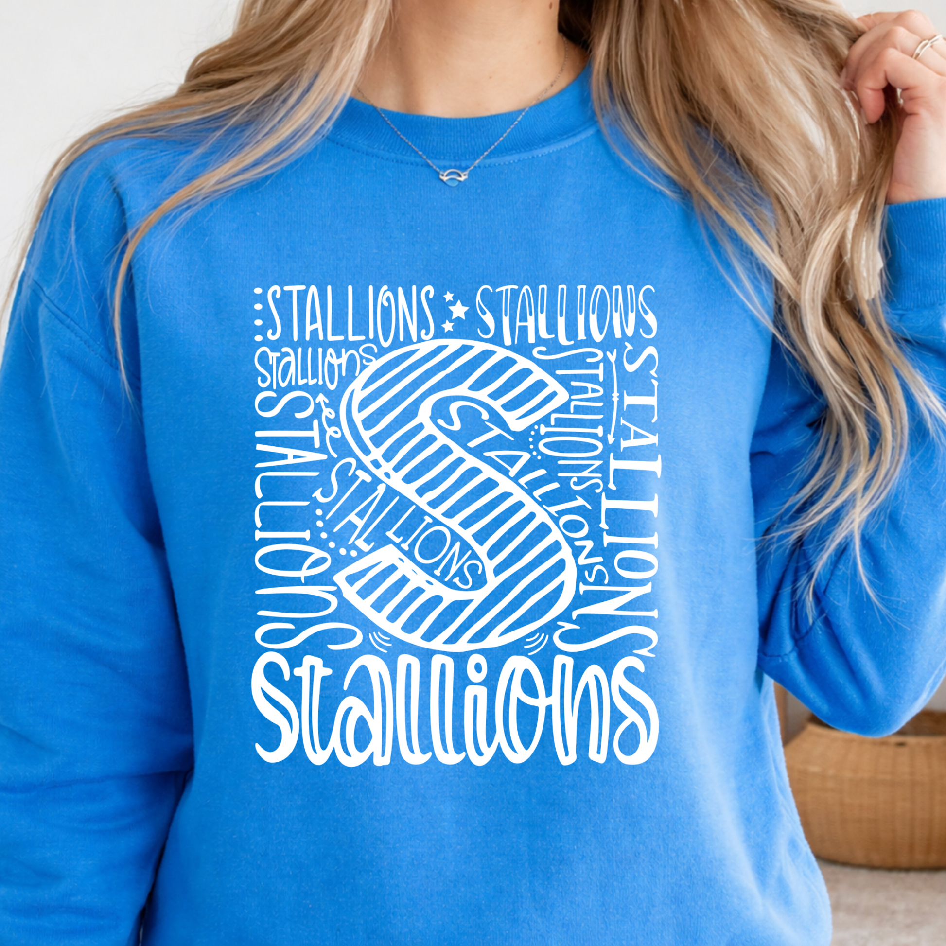 A woman wearing a bright blue crewneck sweatshirt with a large white graphic print on the front featuring the word 'STALLIONS' and a stylized letter 'S'.
