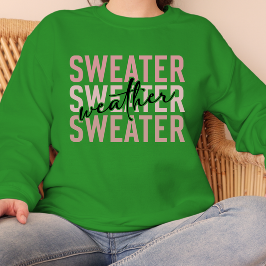 Green sweatshirt with 'Sweater Weather Sweater' text worn by a person sitting on a wicker chair.  Sweater Weather - Cute and Chic Minimalist Fall Crewneck Cozy Sweater