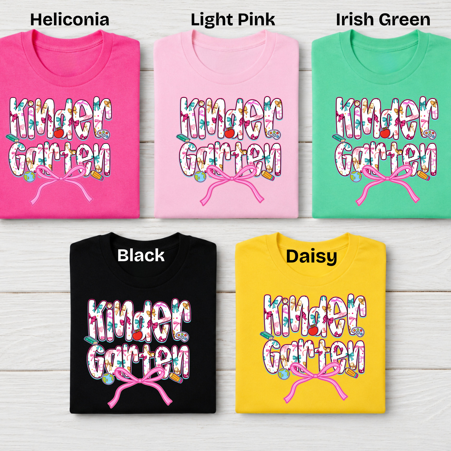 Five folded graphic T-shirts shown on a light wood background, labeled Heliconia, Light Pink, Irish Green, Black, and Daisy. Each shirt features a colorful floral 'Kinder Garten' text design with a pink bow motif.