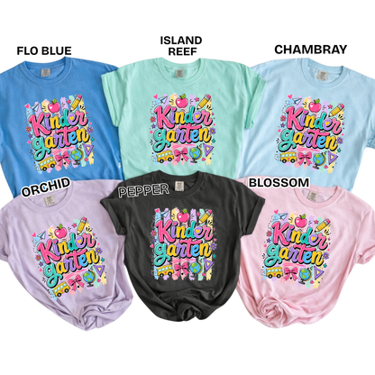 Six graphic T-shirts in different colors are arranged on a white background with text labels naming the shades: FLO BLUE, ISLAND REEF, CHAMBRAY, ORCHID, PEPPER, and BLOSSOM. Each shirt has a colorful retro-style 'Kinder Garden' graphic printed on the front with playful illustrations and text.