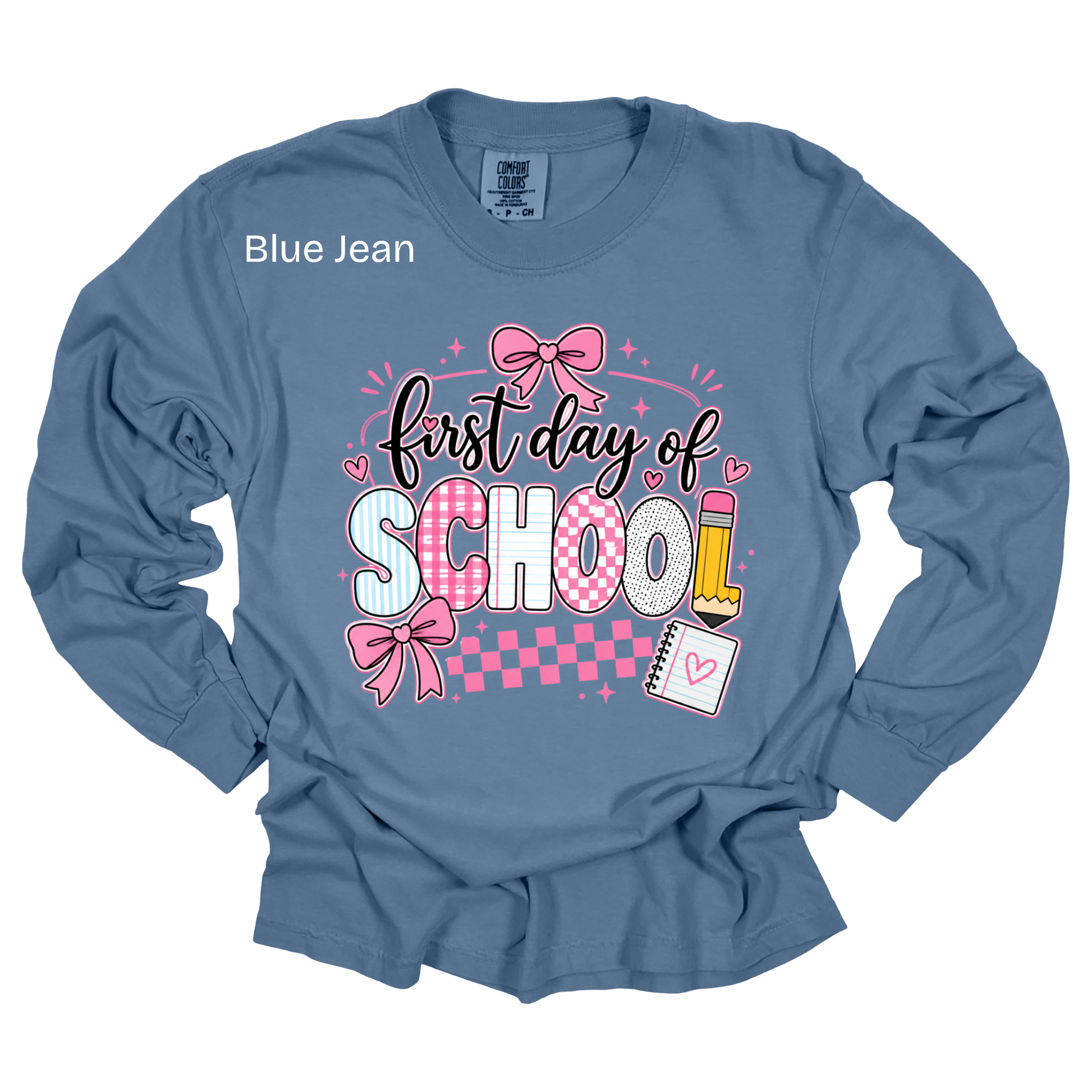 A blue long-sleeve t-shirt with a 'first day of SCHOOL' graphic on the front, featuring pink bows, checkered patterns, and school-themed illustrations, shown on a white background.