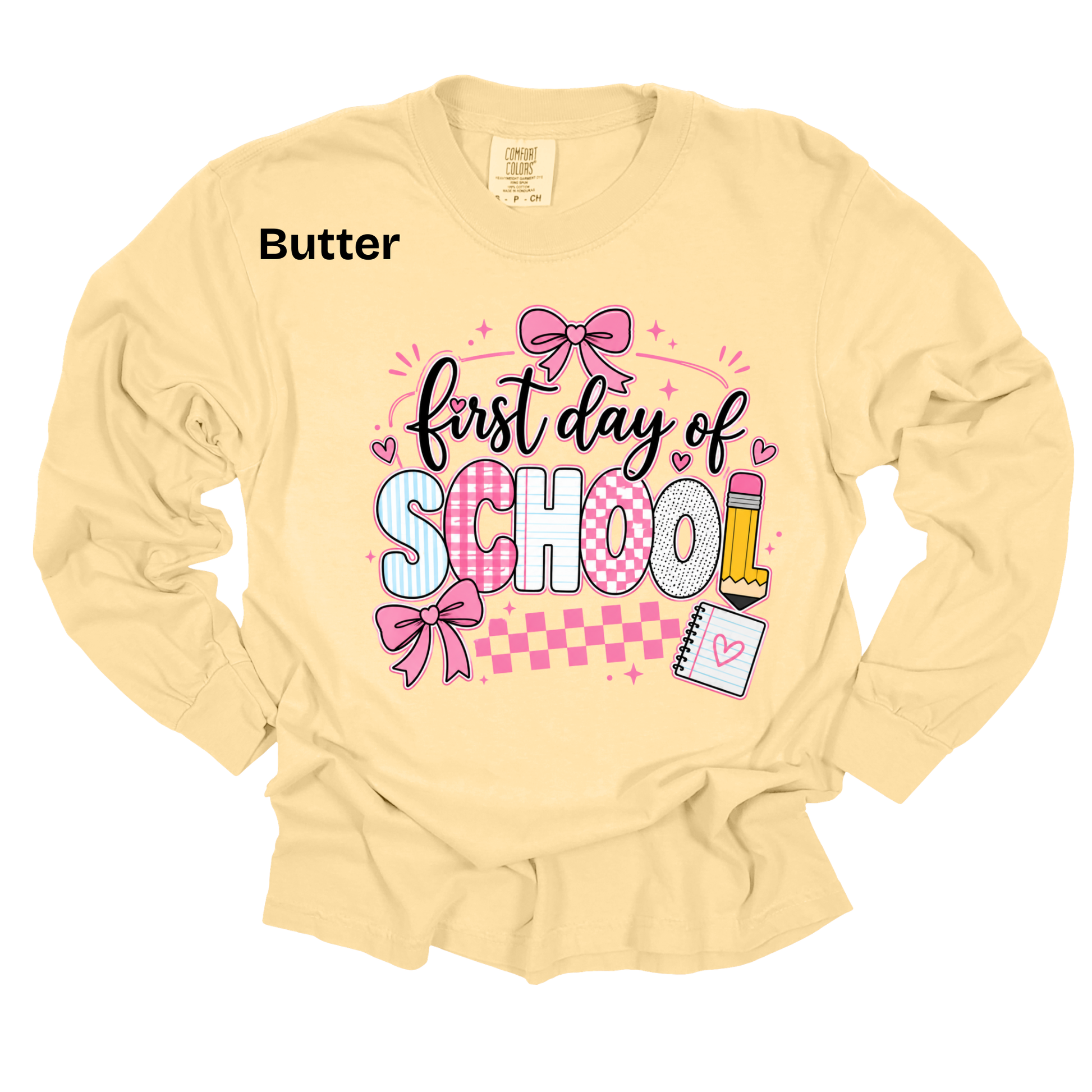 A pale butter-yellow long-sleeve t-shirt with a graphic on the front reading 'first day of SCHOOL' in black script and block letters, decorated with pink bows, hearts, a pencil, and a checkered stripe. The word 'Butter' is printed in black near the upper left chest.