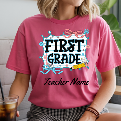 A woman wearing a pink graphic t-shirt with a 'FIRST GRADE Teacher Name' design, sitting indoors next to a drink.
