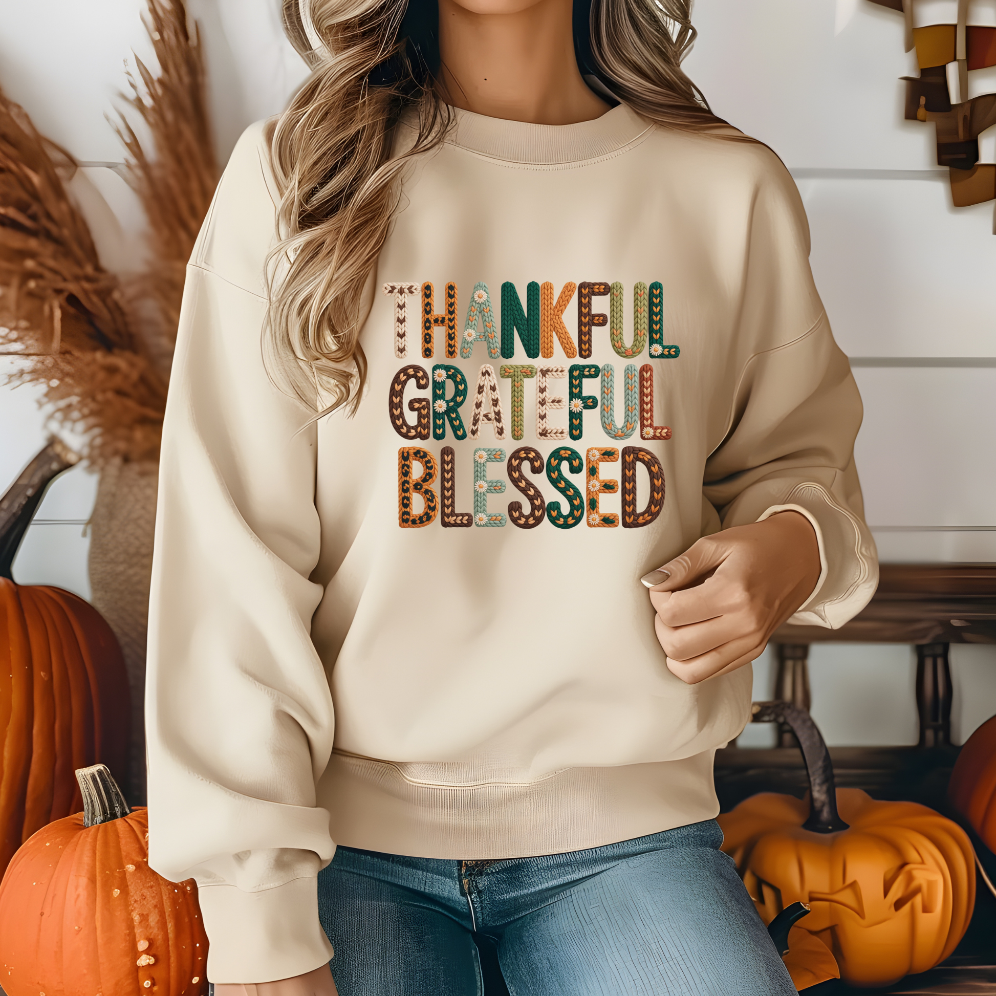 Person wearing a beige sweatshirt with 'Thankful Grateful Blessed' text in a fall-themed setting with pumpkins.