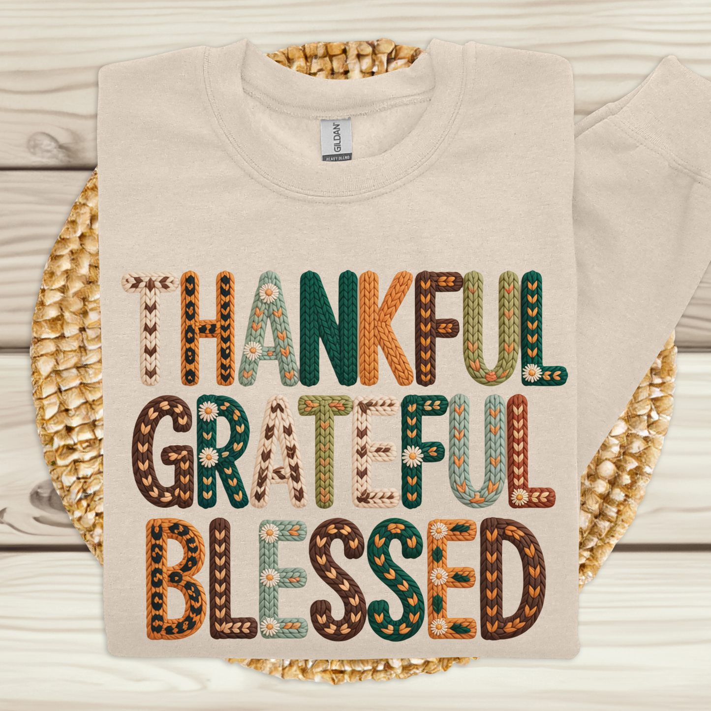 Beige sweatshirt with 'Thankful Grateful Blessed' text in colorful letters on a woven mat.