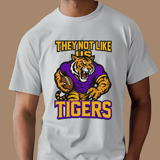 Gray t-shirt with a tiger graphic and text on a brown background Tigers Mascot Shirt - Bold Tigers They Not Like Us Game Day Spirit Tee
