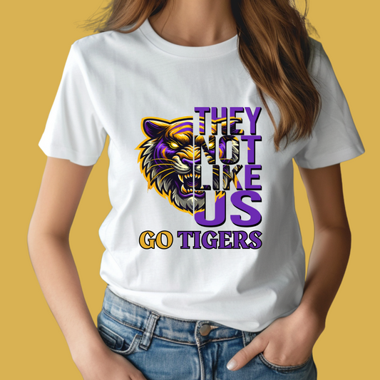 Person wearing a white t-shirt with a tiger graphic and text on a yellow background Tigers Mascot Shirt - Bold Tigers They Not Like Us Team Pride Tee