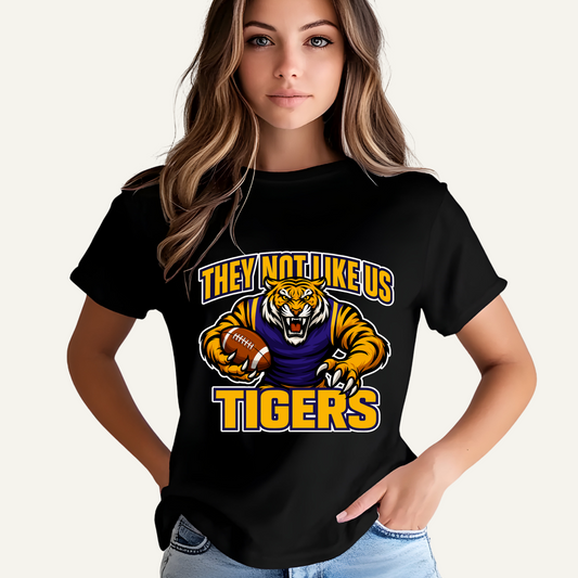 Person wearing a black t-shirt with a tiger graphic and text on a plain  Tigers Mascot T-shirt - Tigers They Not Like Us Game Day Spirit Tee 