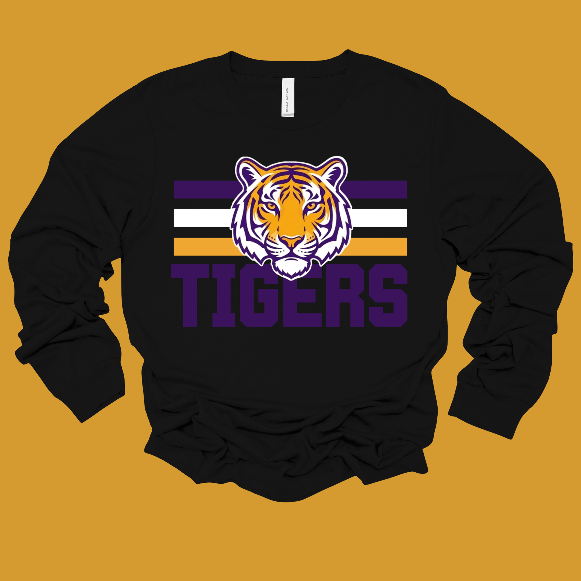 A black long-sleeve crewneck sweatshirt featuring a purple, white, and orange tiger mascot graphic with the word 'TIGERS' underneath, displayed flat against a solid mustard yellow background.