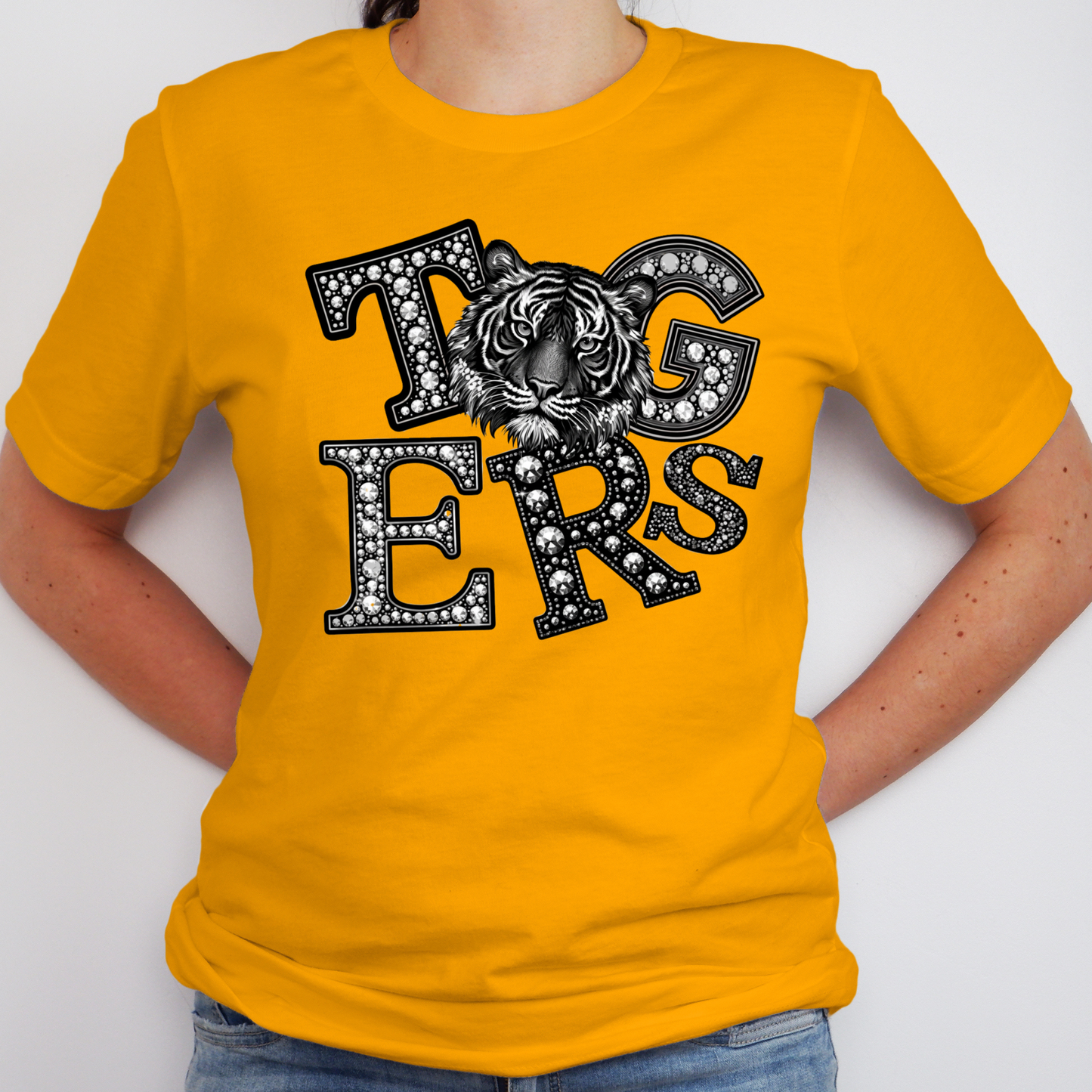 A person wearing a bright yellow short-sleeve T-shirt with a large black-and-white tiger graphic and the word 'Tigers' across the chest, paired with blue jeans against a plain light background.
