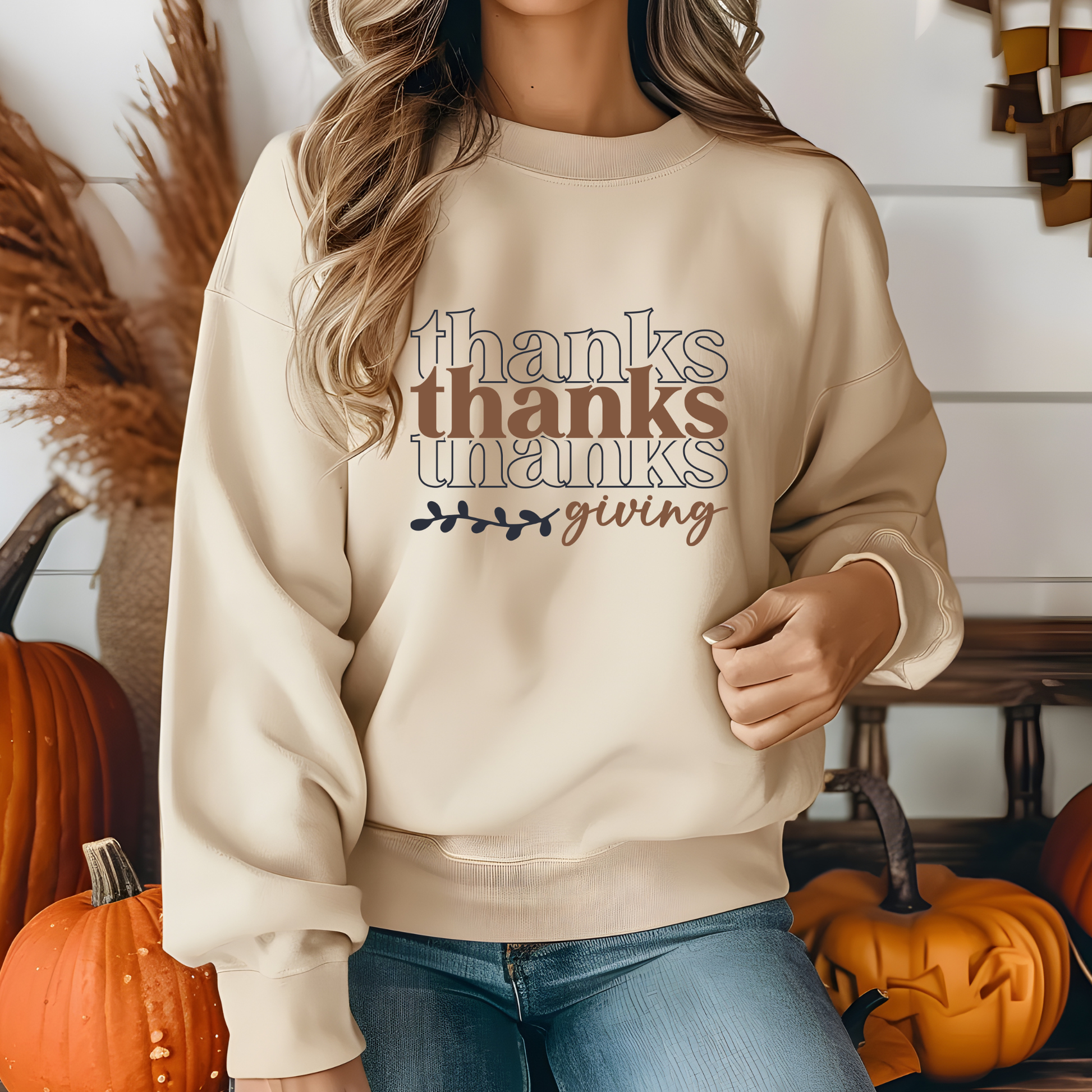 Person wearing a beige sweatshirt with 'thanks giving' text in a home setting with pumpkins.