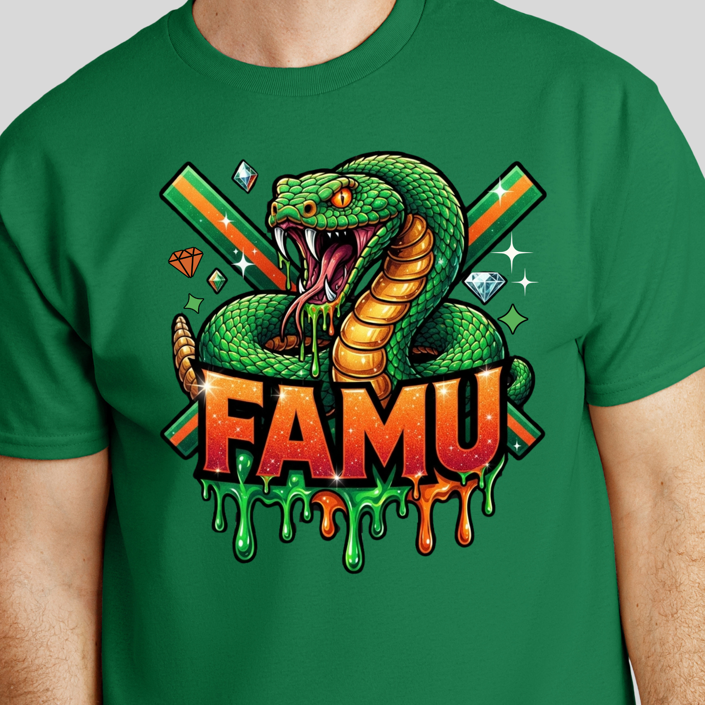 A green short-sleeve crewneck t-shirt featuring a large graphic print of a green cobrasco with an open mouth, dripping slime, and the word 'FAMU' in dripping orange and red letters below it, with crossed green and orange bars in the background.