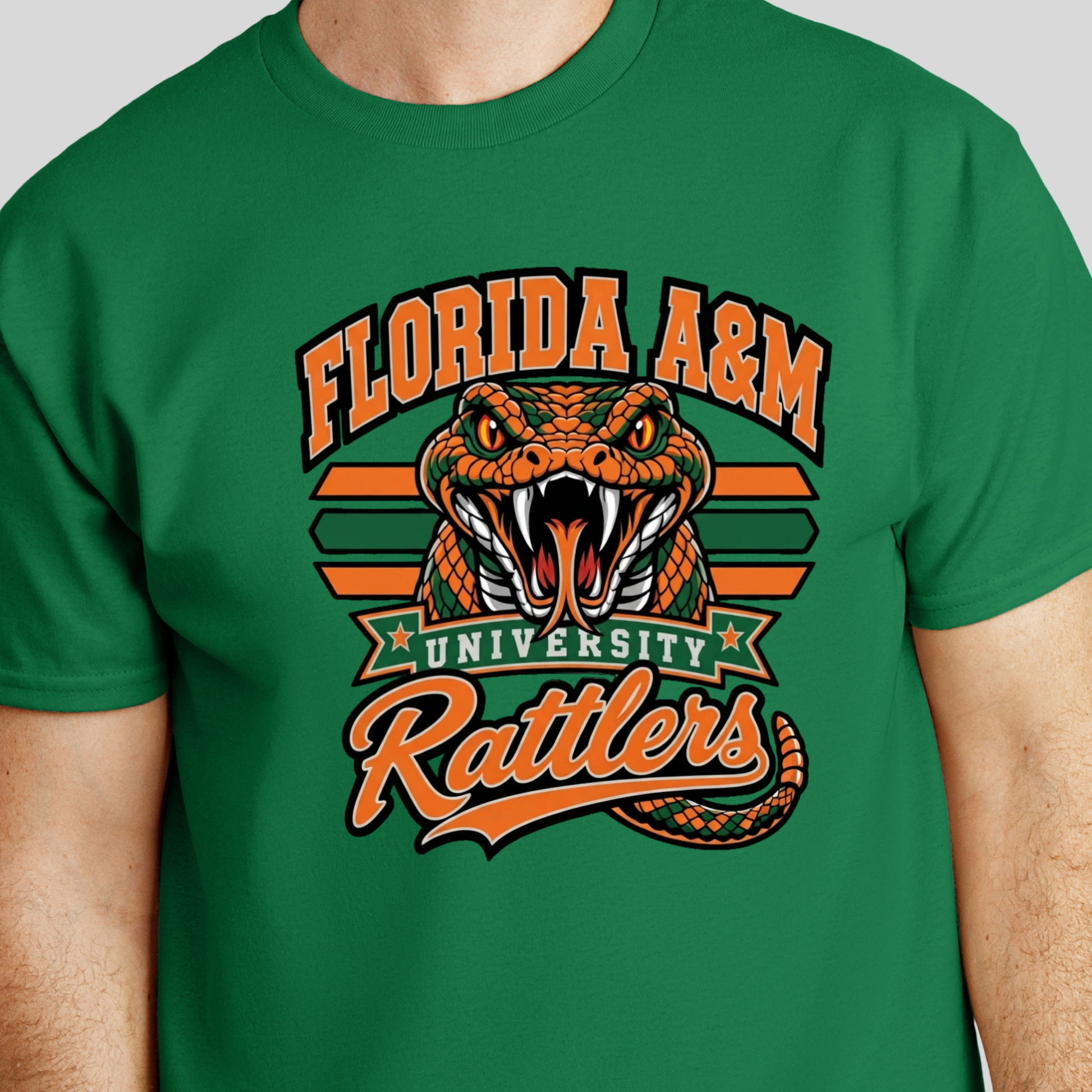 A green short-sleeve crewneck t-shirt featuring a large graphic print of a green cobrasco with an open mouth, dripping slime, and the word 'FAMU' in dripping orange and red letters below it, with crossed green and orange bars in the background.