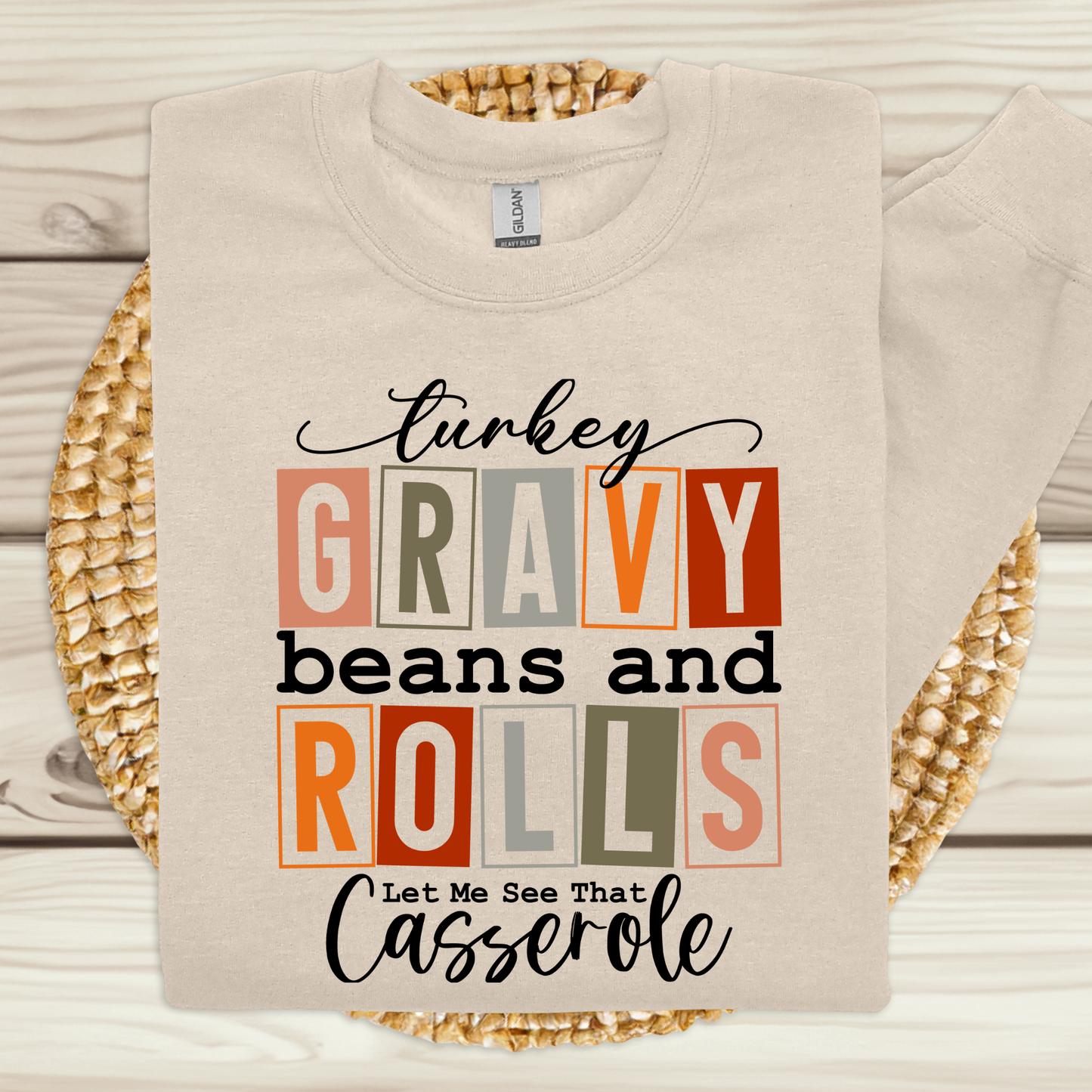 Beige sweatshirt with Thanksgiving-themed text design on a wooden surface.