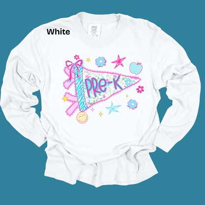 A white long-sleeve t-shirt with a colorful 'Pre-K' ribbon pennant graphic, displayed flat against a solid teal background. The text 'White' is printed in black near the collar, and the shirt features a variety of pastel graphic elements including stars, flowers, and a smiley face.