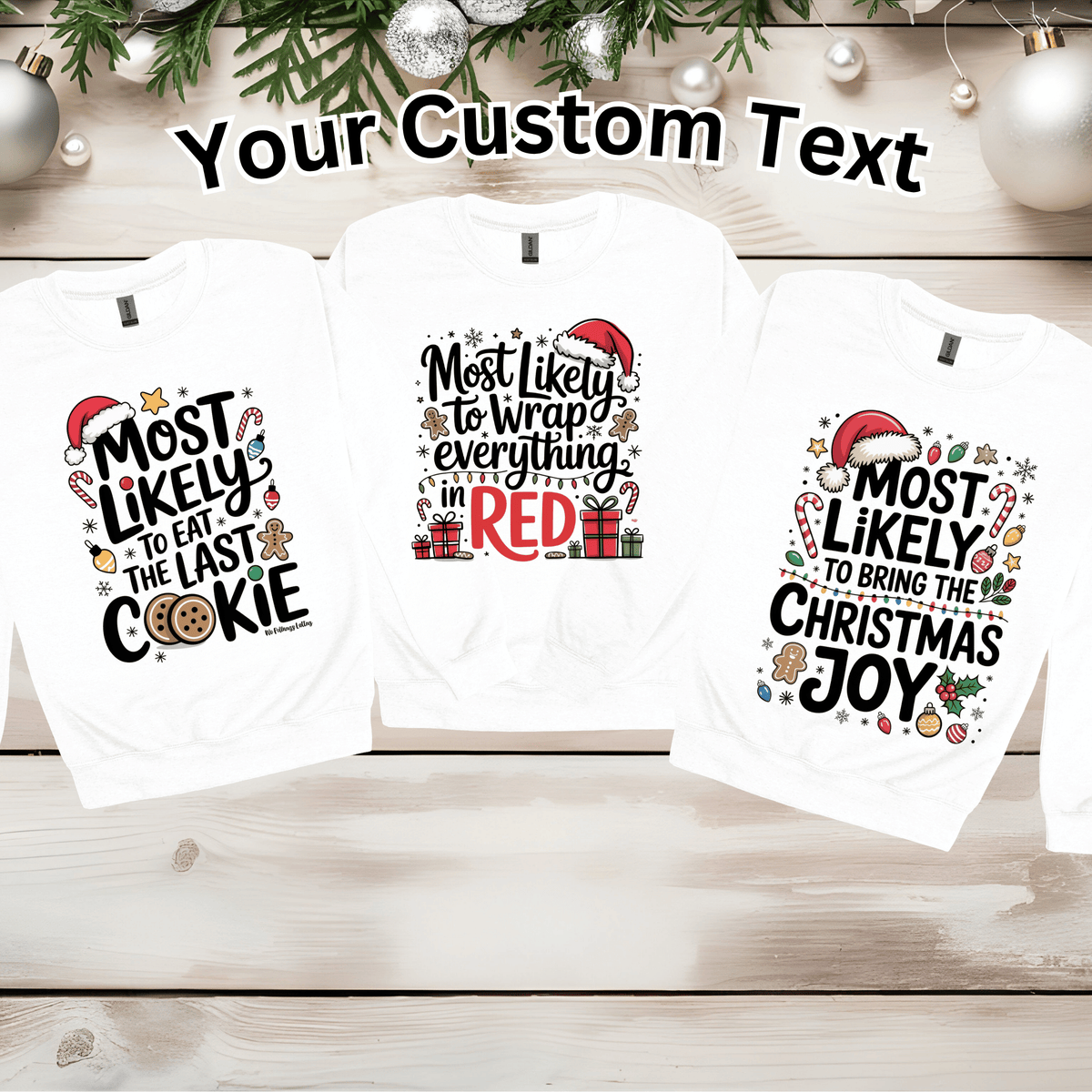 Three white long-sleeve graphic t-shirts displayed on a light wood plank background with holiday greenery and silver ornaments. The shirts feature different Christmas-themed custom text designs: 'Most Likely to Eat the Last Cookie', 'Most Likely to Wrap everything in Red', and 'Most Likely to Bring the Christmas Joy'.