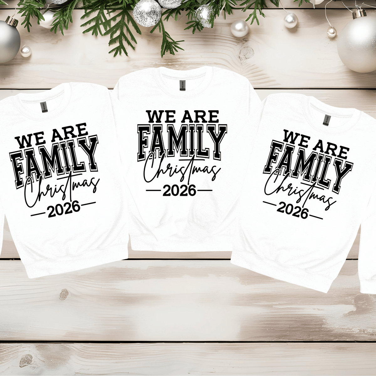 Set of five black matching family t-shirts printed with white 'We Are Family Christmas 2026' collegiate typography on a wooden backdrop.