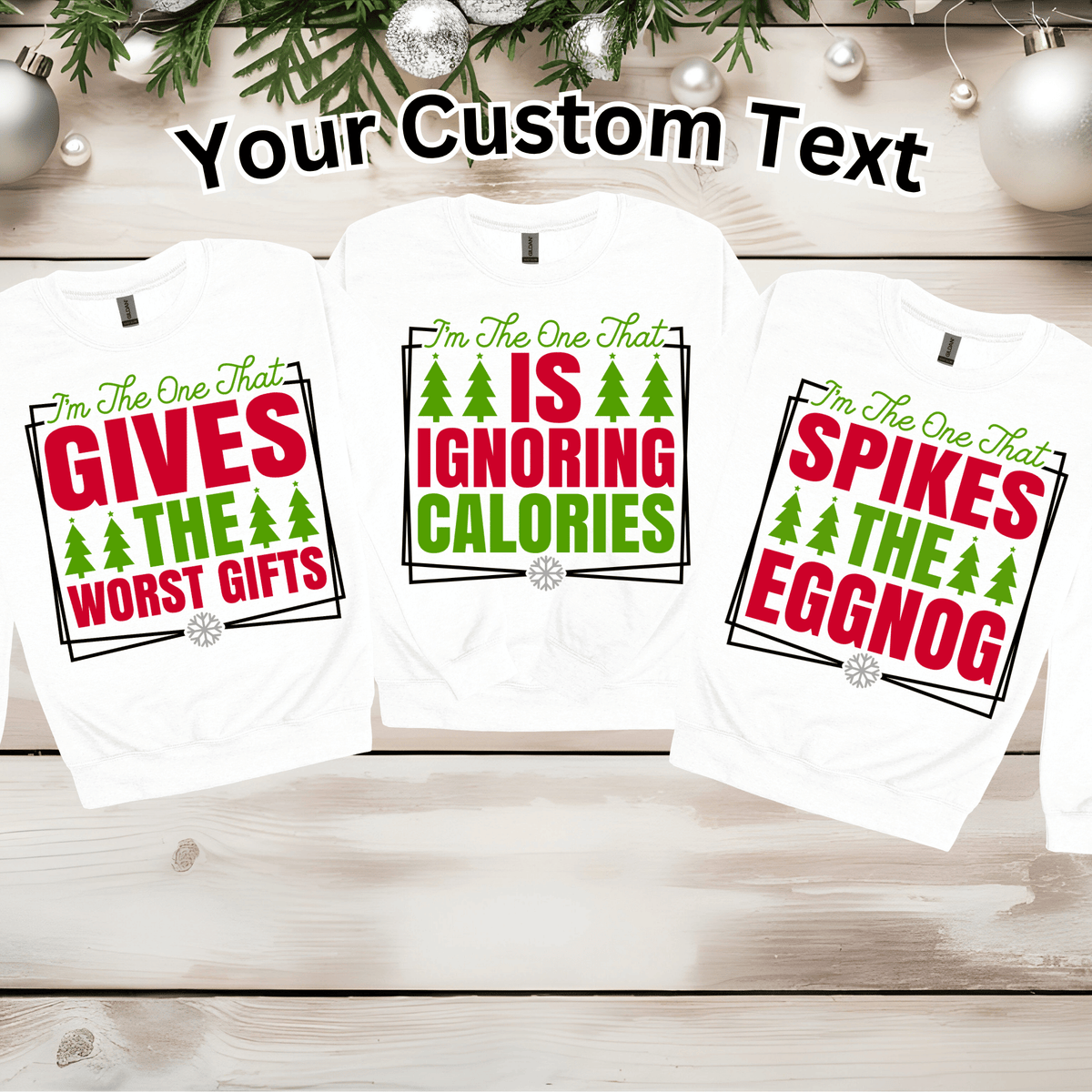 Three white long-sleeve t-shirts with custom Christmas-themed text graphics displayed on a light wood background with holiday decorations. The shirts feature red and green text and pine tree illustrations, with the top of the image including the text 'Your Custom Text'.