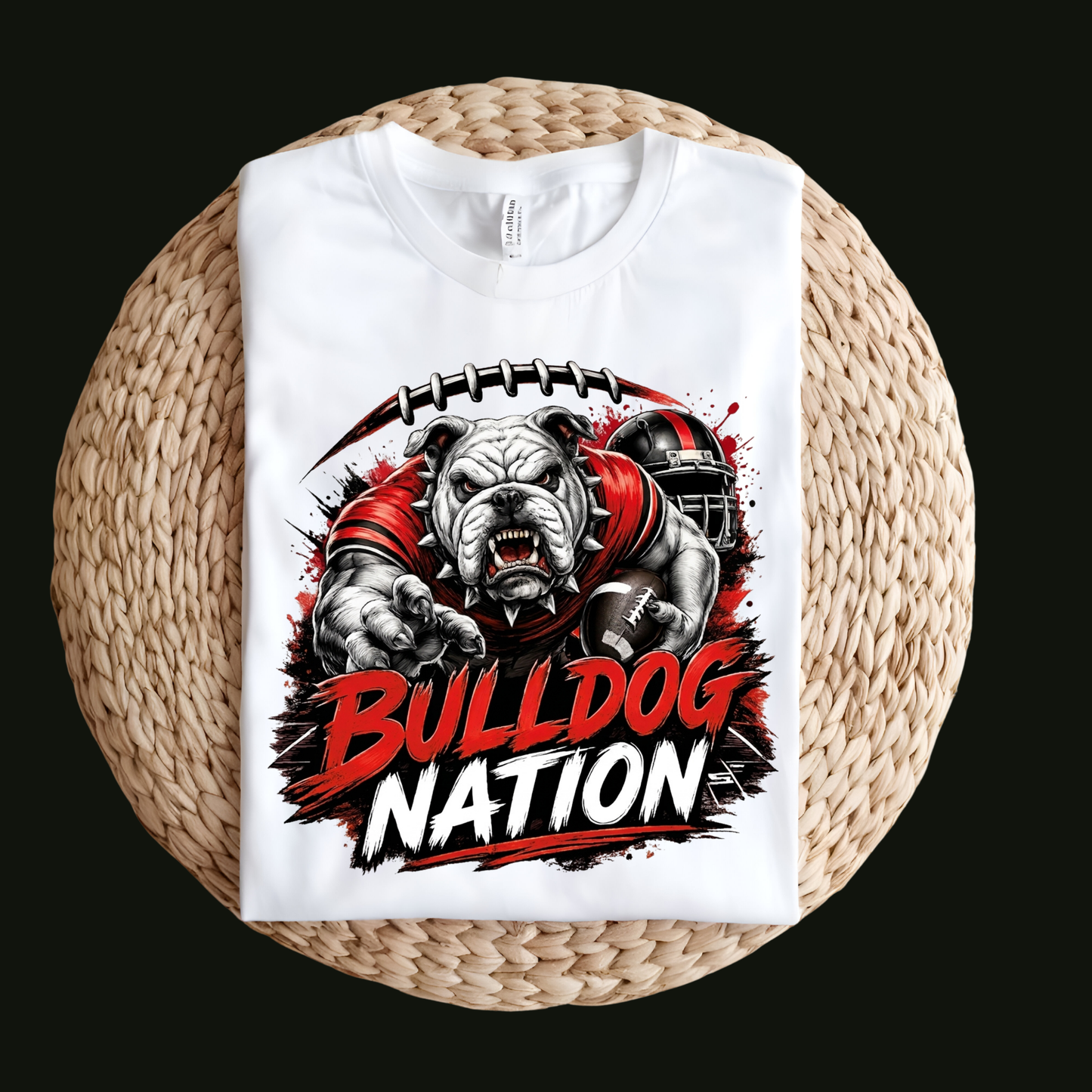 A white short-sleeve T-shirt laid flat on a round woven straw mat against a black background. The shirt has a large front graphic reading “WE ARE Bulldogs” in distressed red, black, and white lettering.