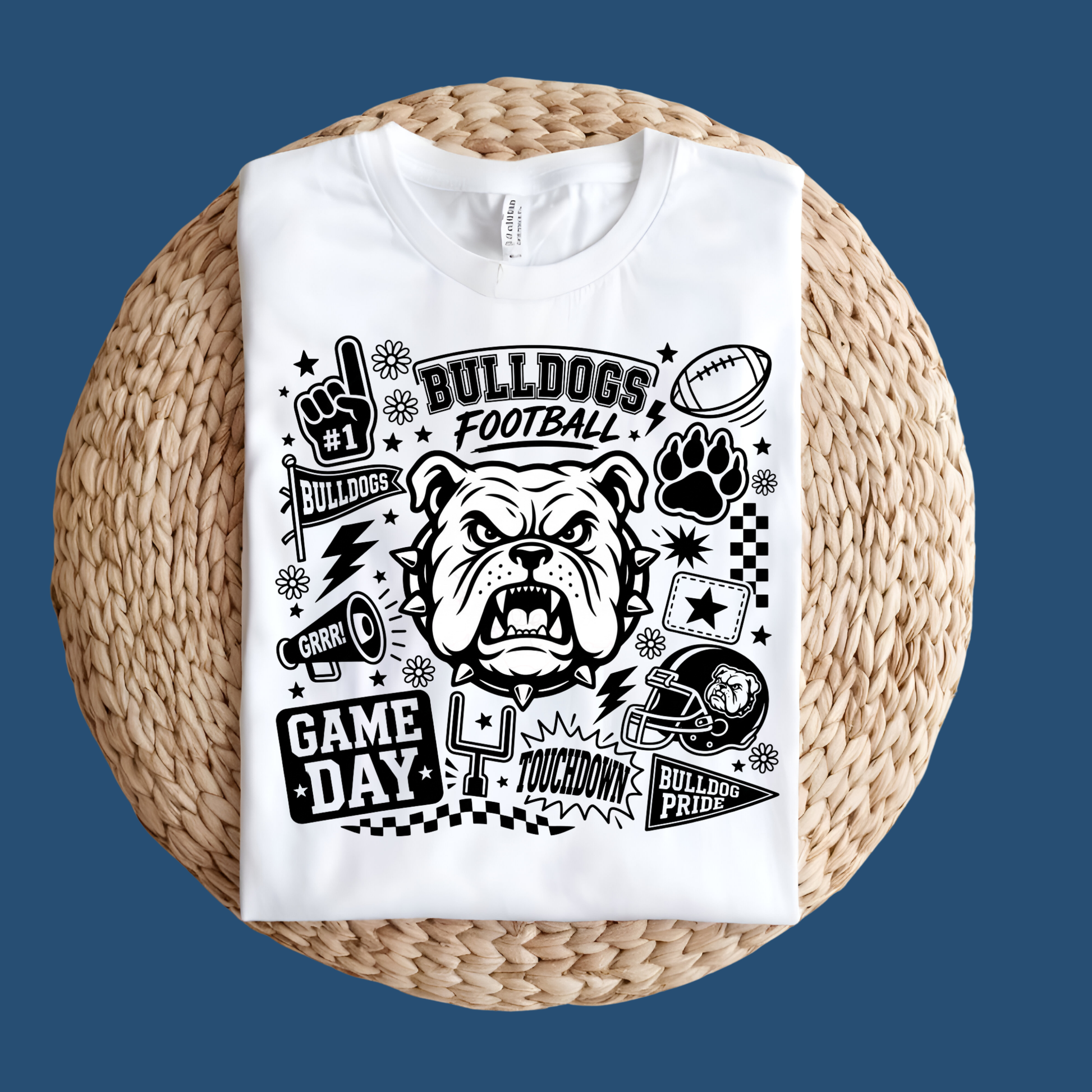 A white short-sleeve T-shirt laid flat on a round woven straw mat against a black background. The shirt has a large front graphic reading “WE ARE Bulldogs” in distressed red, black, and white lettering.