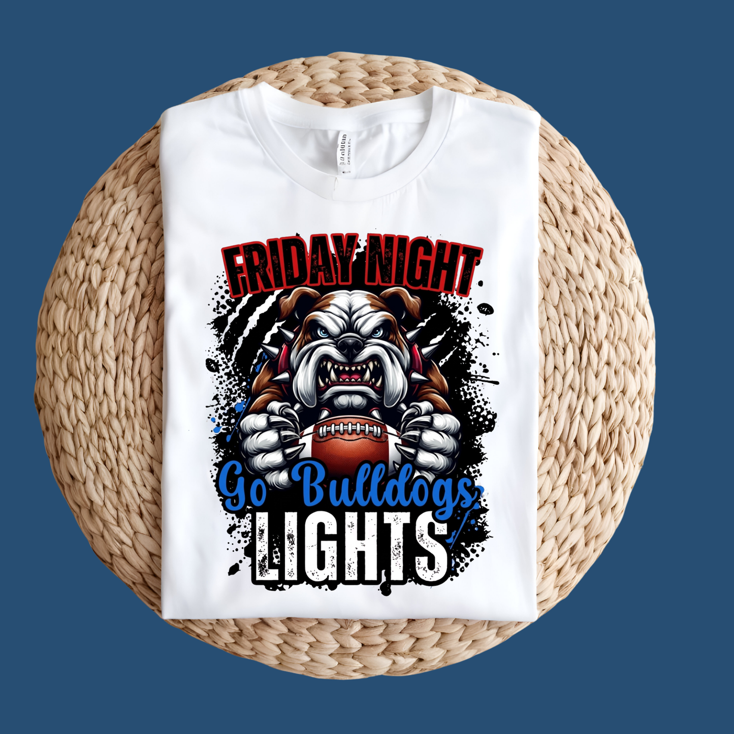 A white short-sleeve T-shirt laid flat on a round woven straw mat against a black background. The shirt has a large front graphic reading “WE ARE Bulldogs” in distressed red, black, and white lettering.