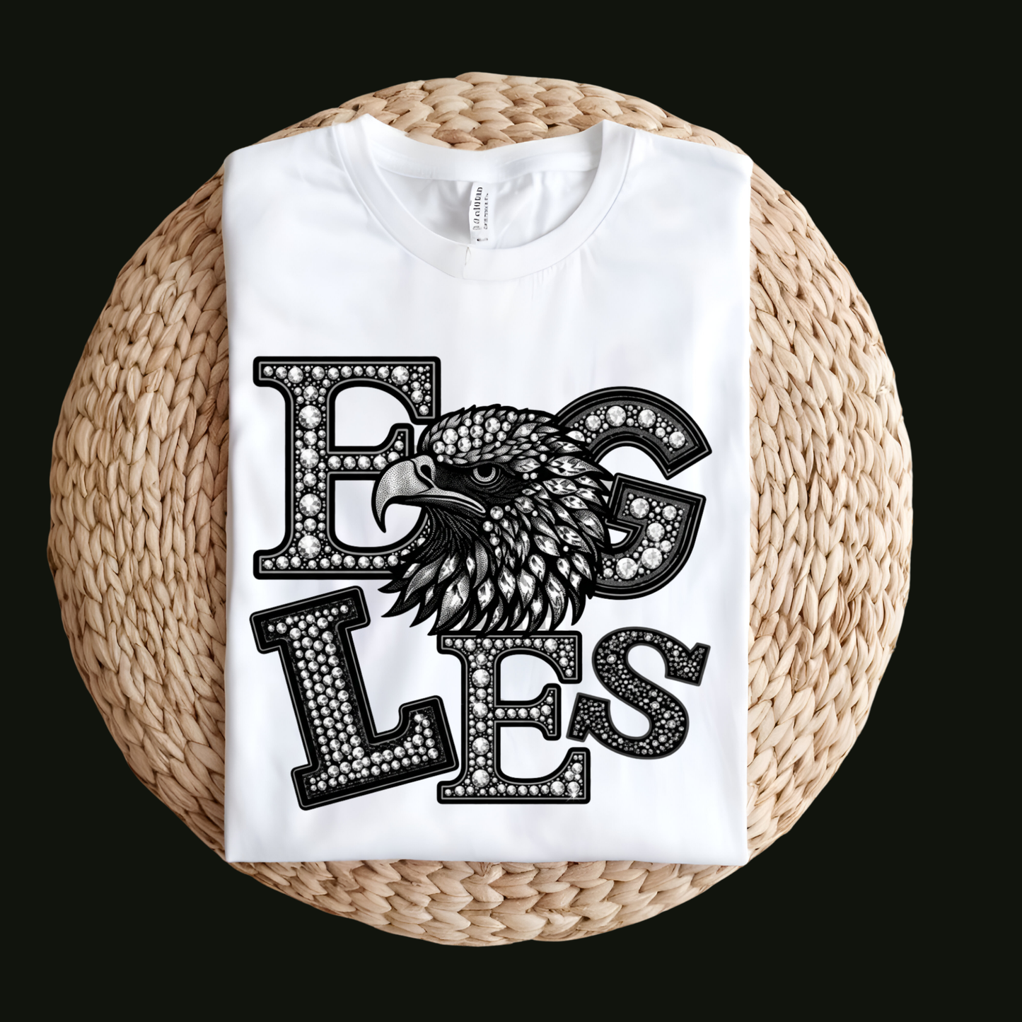 A white short-sleeve T-shirt laid flat on a round woven straw mat against a black background. The shirt has a large front graphic reading “WE ARE Bulldogs” in distressed red, black, and white lettering.