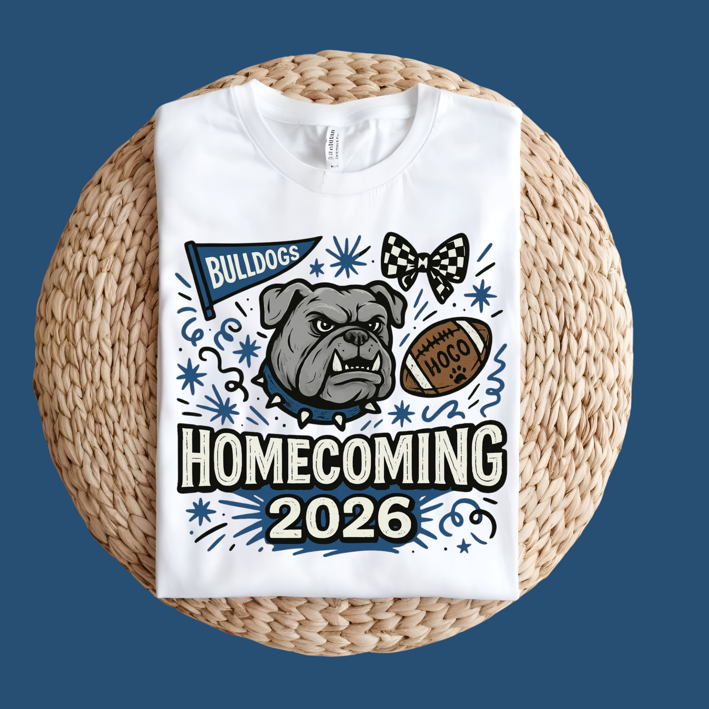 A white short-sleeve T-shirt laid flat on a round woven straw mat against a black background. The shirt has a large front graphic reading “WE ARE Bulldogs” in distressed red, black, and white lettering.