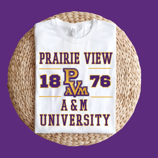 A folded white t-shirt with a purple and gold 'Prairie View 1876 A&M University' graphic, displayed on a round woven straw mat against a solid purple background.