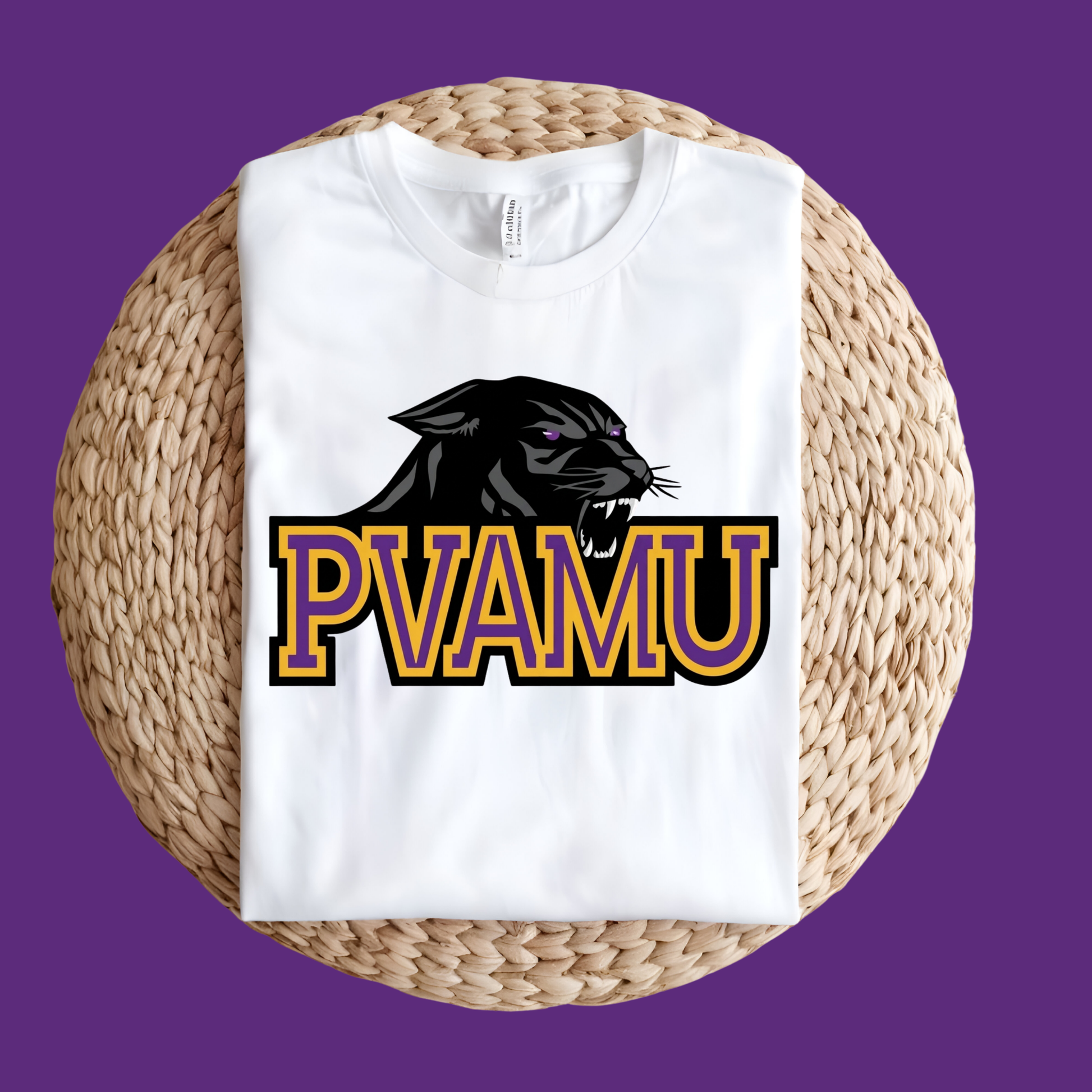 A white short-sleeve T-shirt laid flat on a round woven straw mat, featuring a large graphic of a purple and gold football player with the text 'PRAIRIE VIEW A&M PANTHERS' on the front, set against a solid purple background.