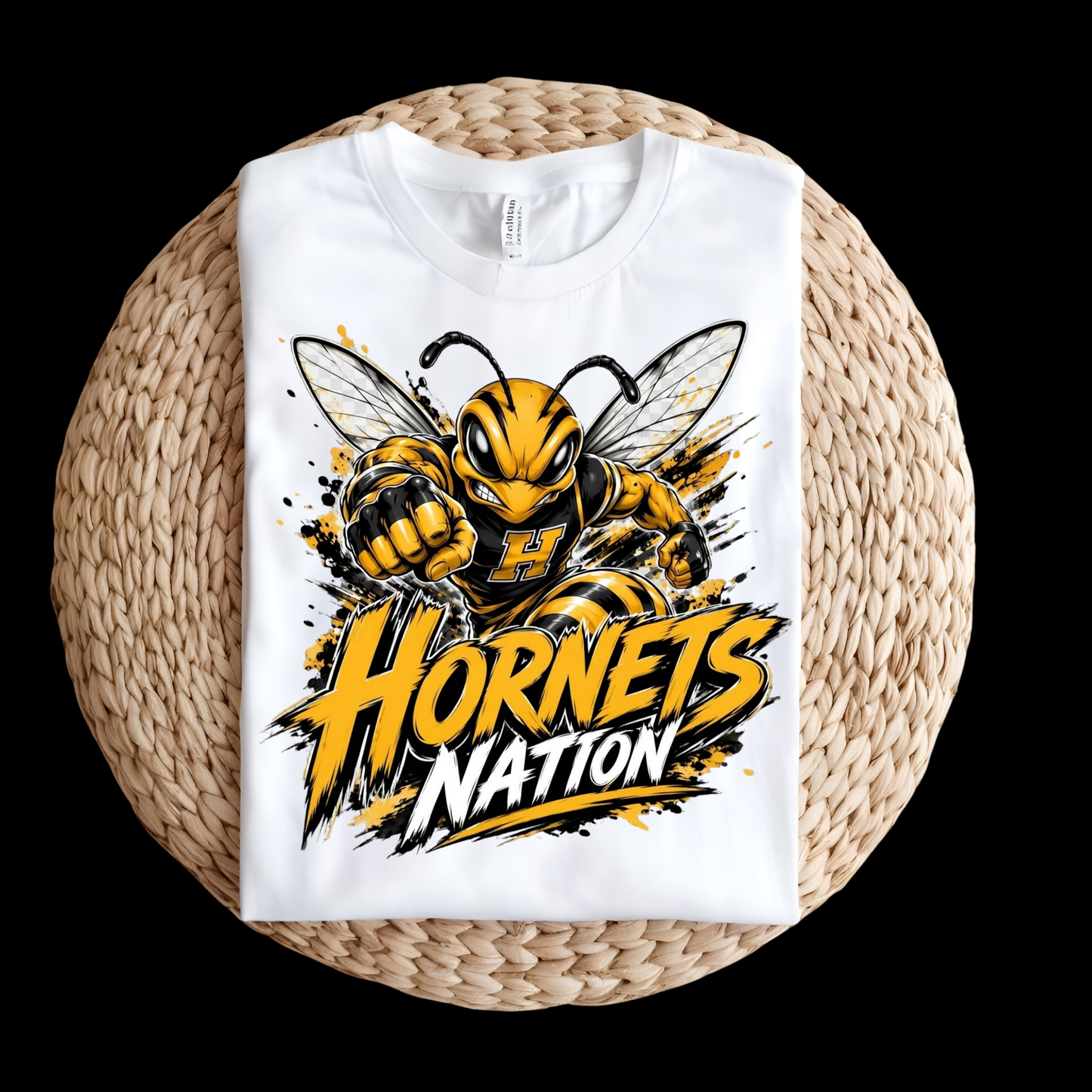A white short-sleeve T-shirt laid flat on a round woven straw mat, featuring a large yellow and black hornet graphic with the words 'Hornets Nation' on the front.