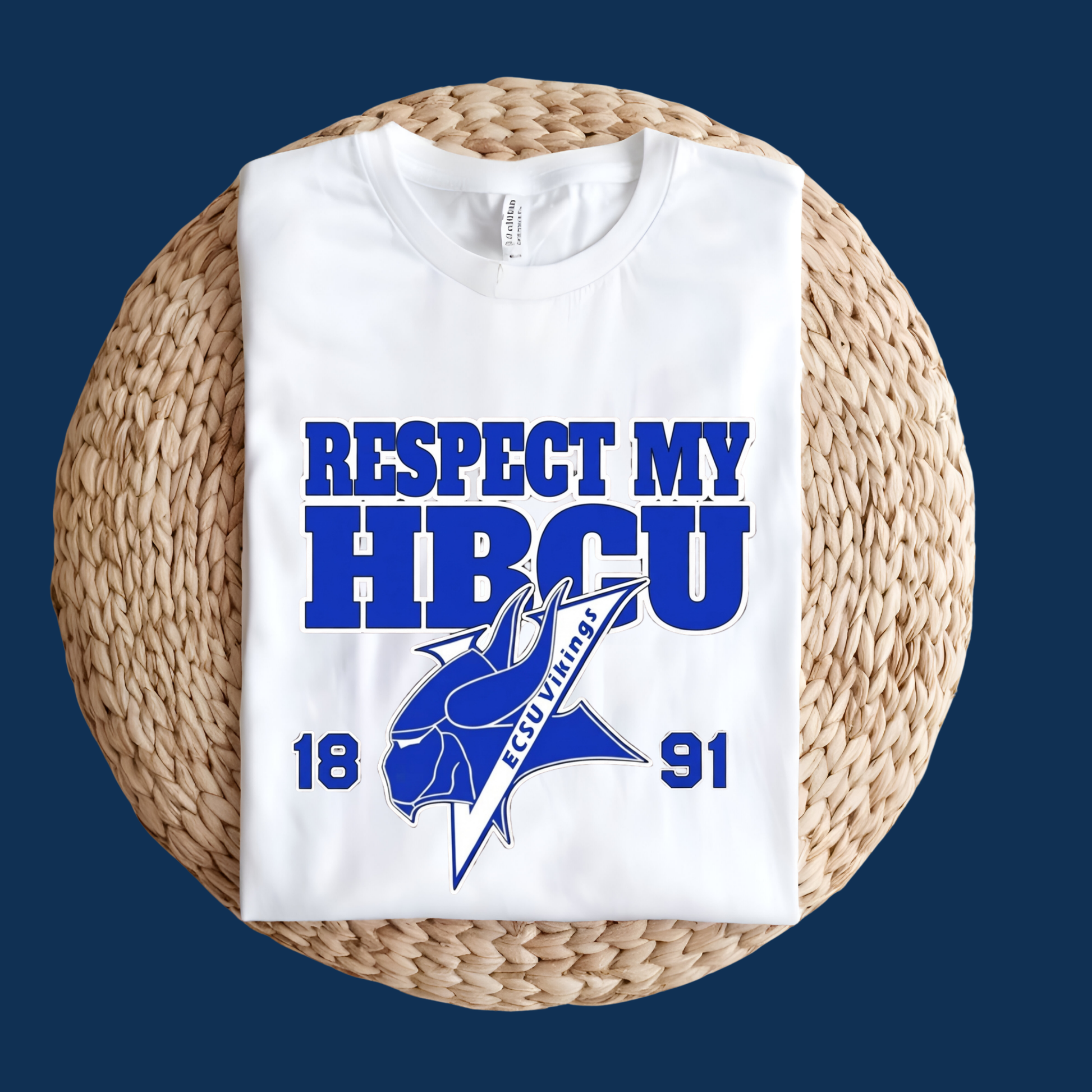 A white short-sleeve T-shirt folded and displayed on a round woven straw mat against a dark blue background. The shirt features a bold blue graphic that reads 'RESPECT MY HBCU' with '1891' and a blue mascot logo in the center.