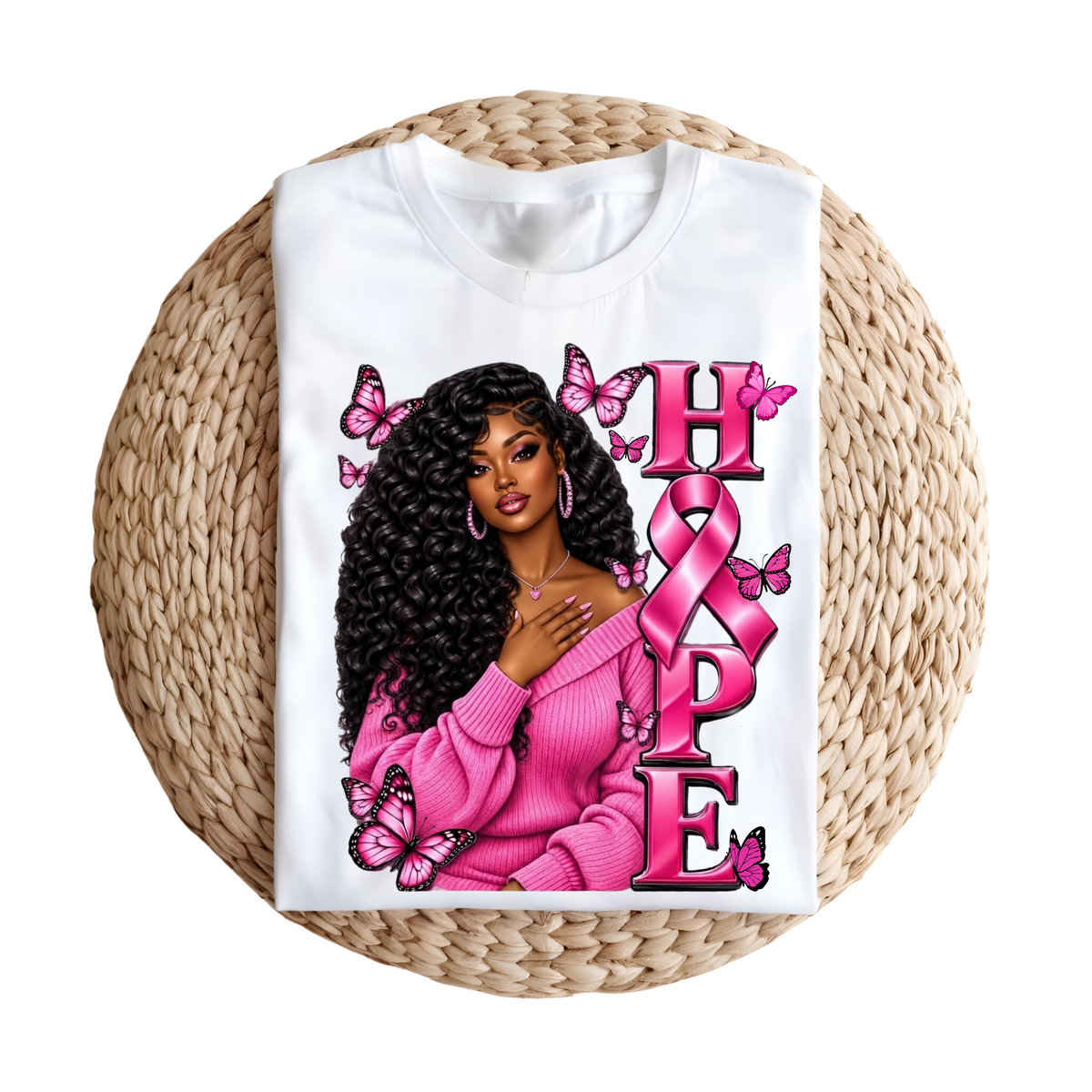 A white short-sleeve T-shirt laid flat on a round woven straw mat, featuring a large pink and black graphic that reads “HOPE” with pink ribbons, butterflies, and hearts.