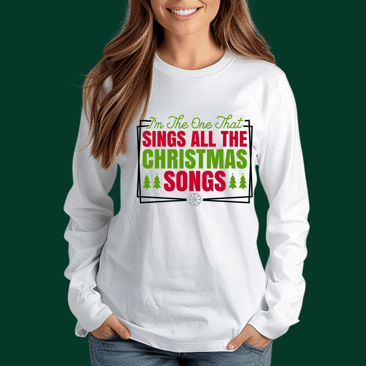 A woman wearing a white long-sleeve t-shirt with a colorful graphic that reads 'I'm The One That SINGS ALL THE CHRISTMAS SONGS' in green and red lettering, set against a solid dark green background.