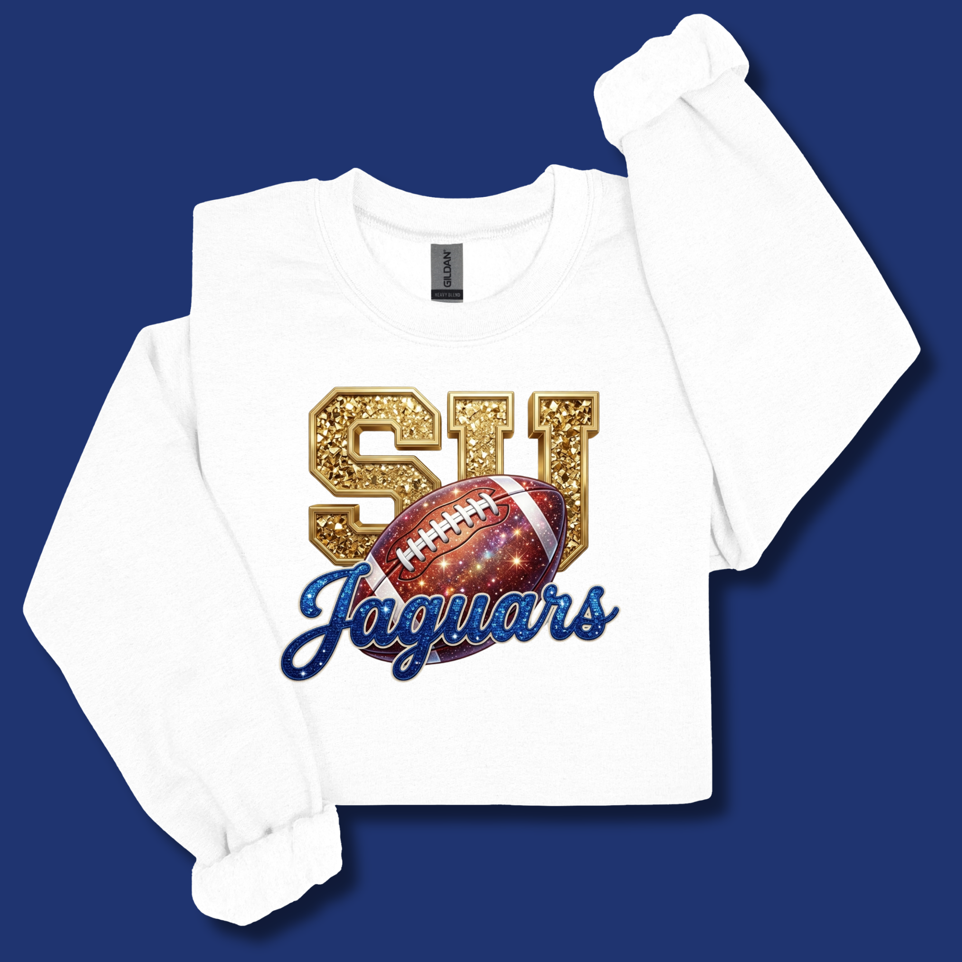 A white long-sleeve t-shirt with a custom graphic print featuring glittery gold 'SU' letters, a red and white football, and the word 'Jaguars' in blue script, displayed on a solid dark blue background.