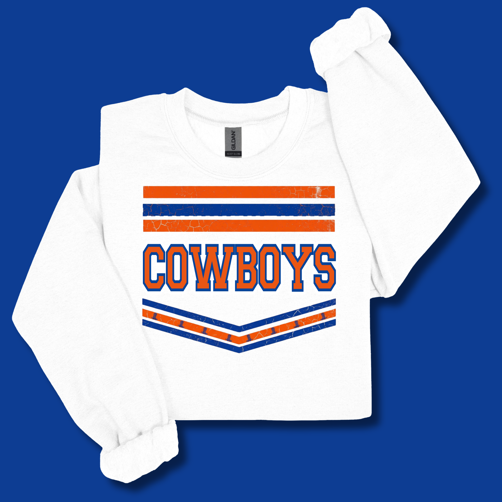 A white long-sleeve t-shirt with a distressed orange and blue 'COWBOYS' graphic on the front, displayed on a solid blue background.