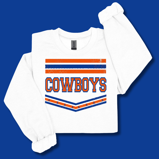 A white long-sleeve t-shirt with a distressed orange and blue 'COWBOYS' graphic on the front, displayed on a solid blue background.