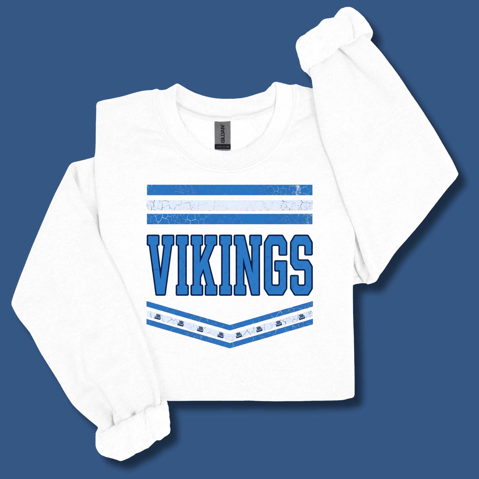 A white long-sleeve t-shirt with a blue graphic print on the front reading 'VIKINGS' inside a chevron design, displayed on a solid blue background.